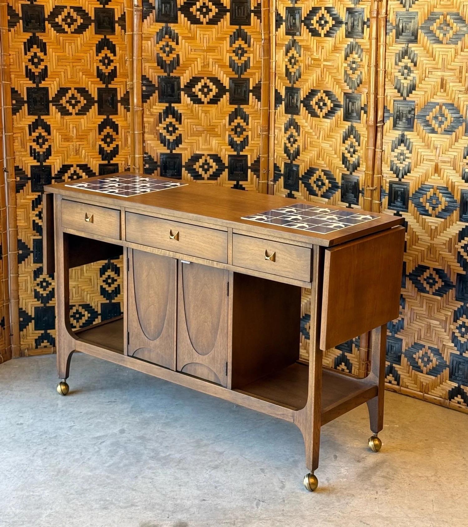 Mid-century rolling bar cart designed by Broyhill, circa 1960s. This seldom seen piece is a part of Broyhill’s Brasilia line, inspired by the architecture of Oscar Niemeyer. Niemeyer used grand arches in his buildings located in the capital of