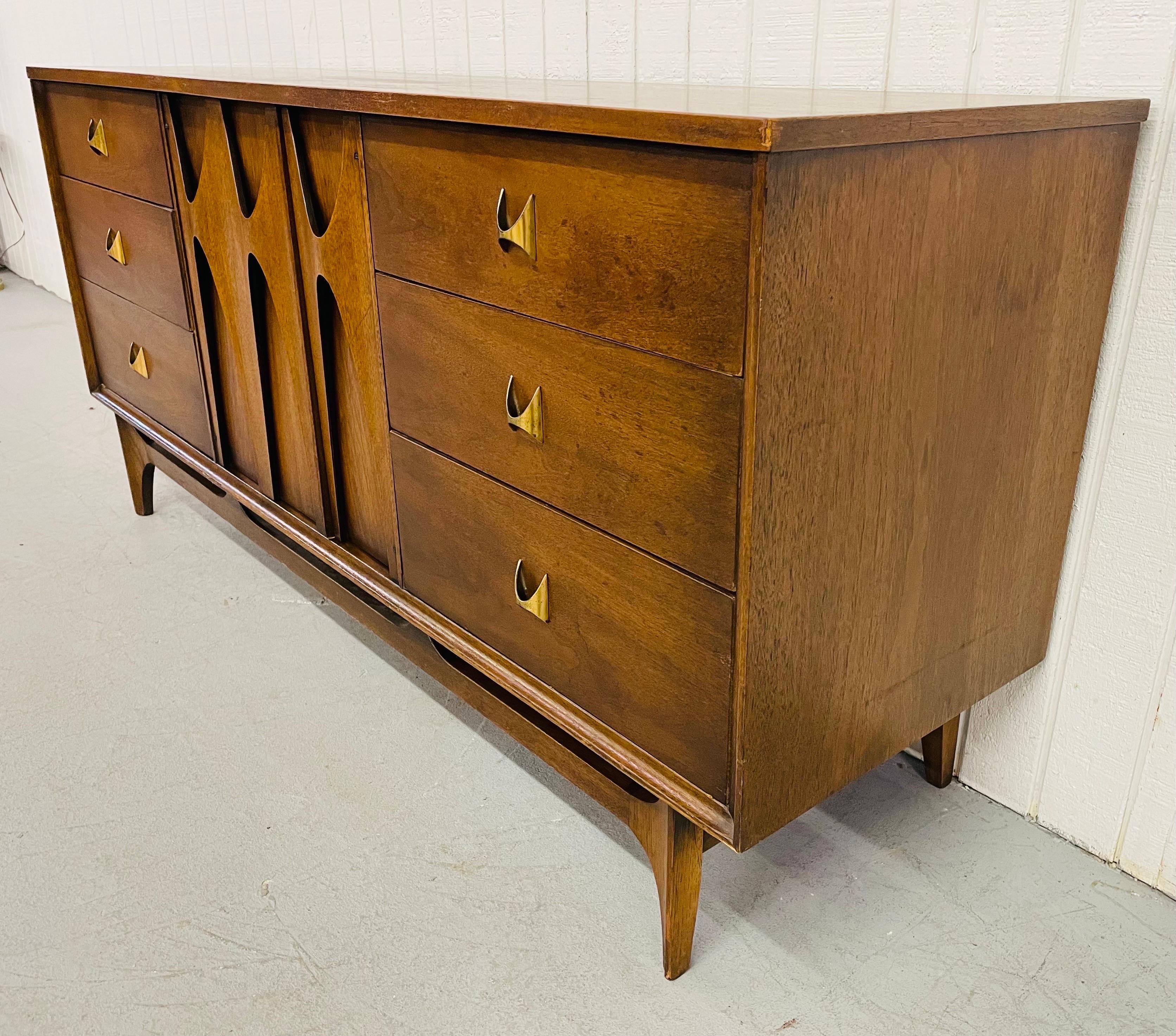 This listing is for a mid-century Broyhill Brasilia walnut triple dresser. Featuring nine drawers for storage, a center door, original Brasilia hardware, and the original tag in the drawer.