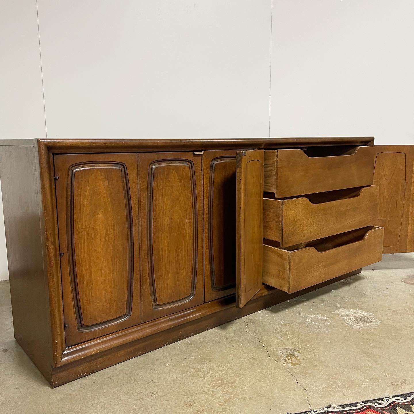 Mid century sideboard by Broyhill. Out of the Emphasis line. Walnut build. Very well built and sturdy! This piece offers double doors with the iconic emphasis design on the front. The left side offers modular shelves for storage. The right side