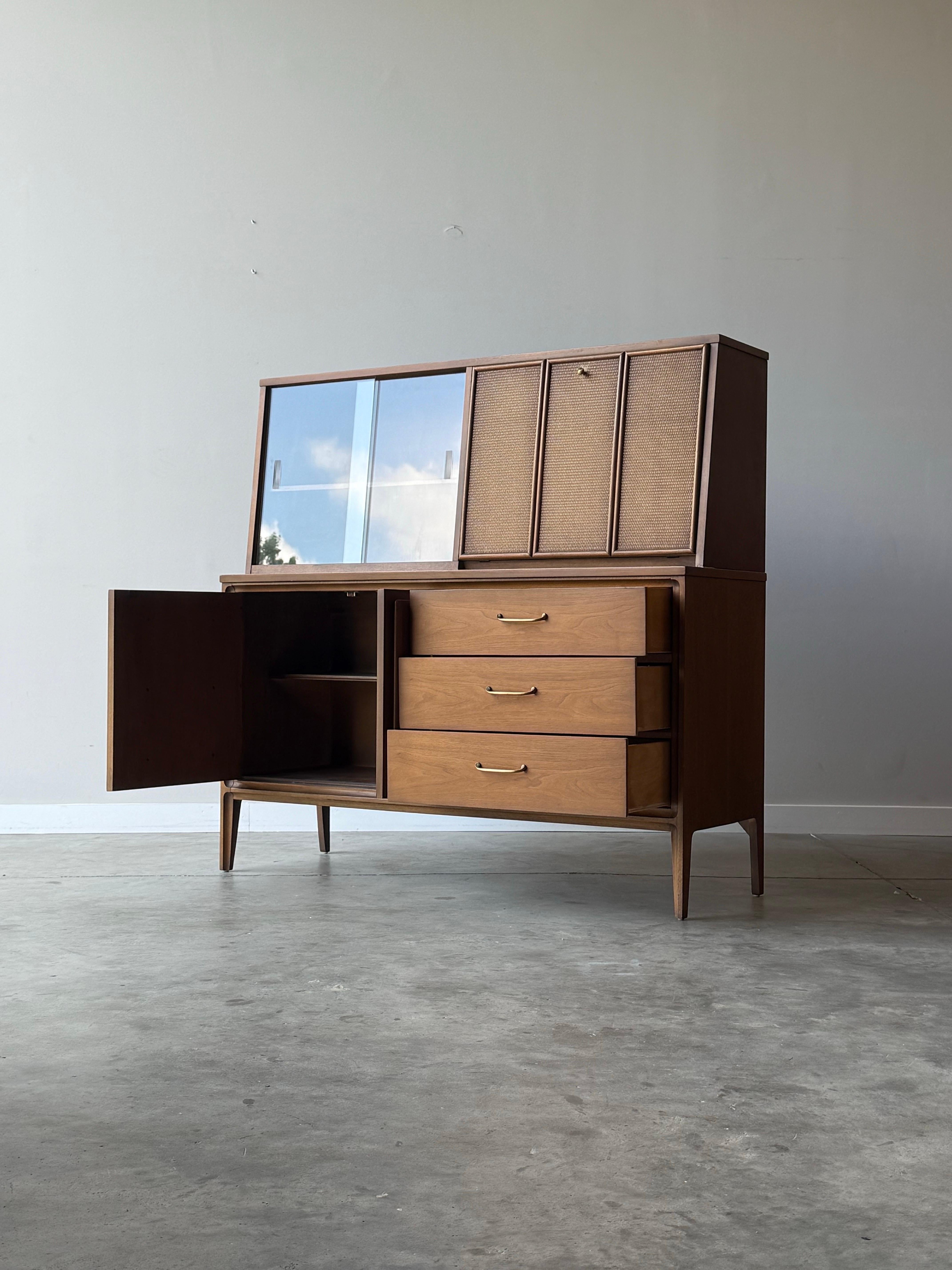 Bar o conigliera di metà secolo prodotto da Broyhill, circa anni '60. Realizzato in noce, presenta due sezioni distinte. La sezione inferiore ha  una serie di tre cassetti sul lato destro con sottili maniglie in ottone. Il lato sinistro presenta due