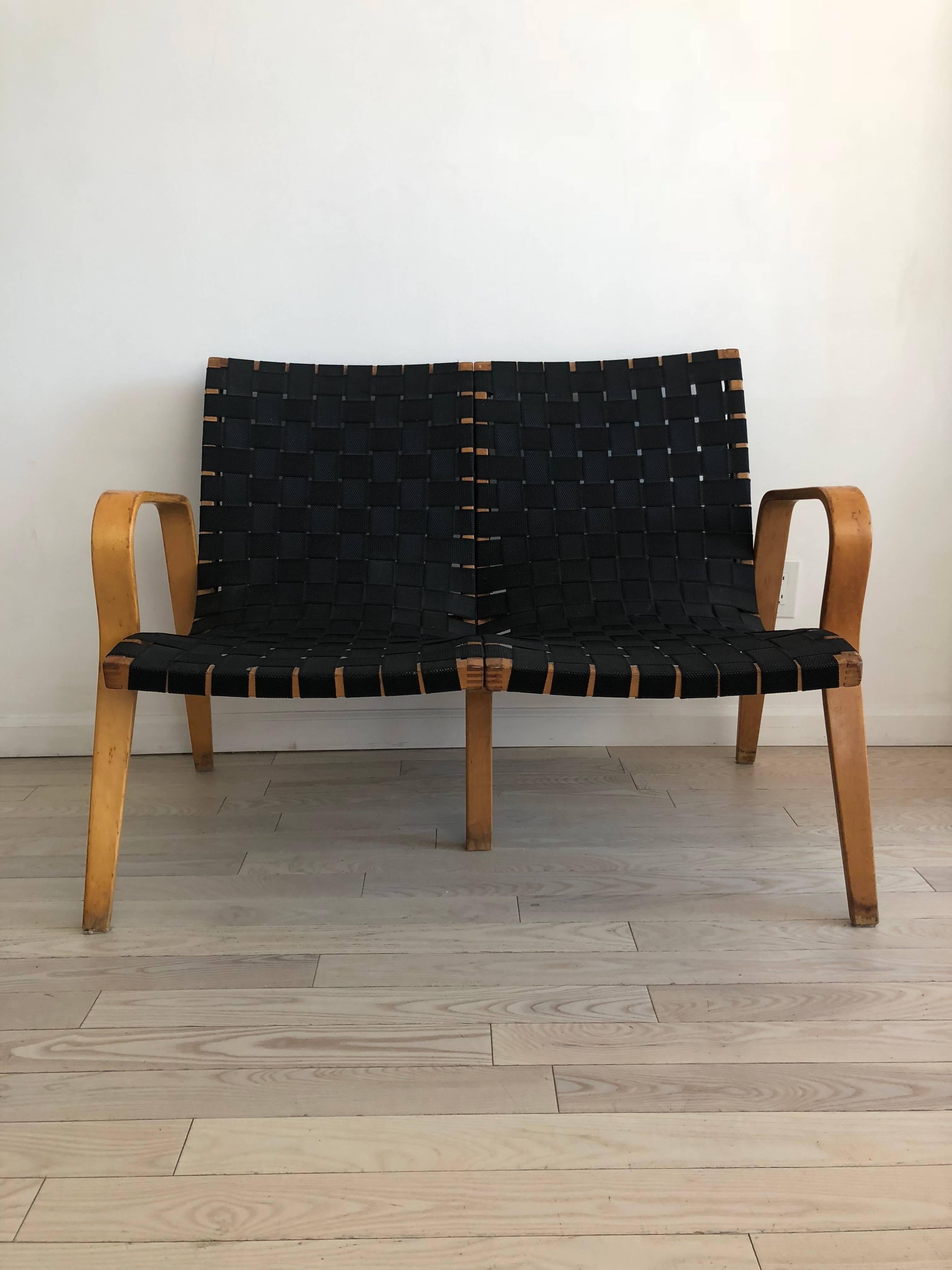 Midcentury Bruno Mathsson style bent birch with black webbing settle. Seats two persons. Pretty bentwood arms with tapered legs. Lounge loveseat! Some mild scuffs, stains and nicks on wood from age and use. Measure: Seat height 16.5