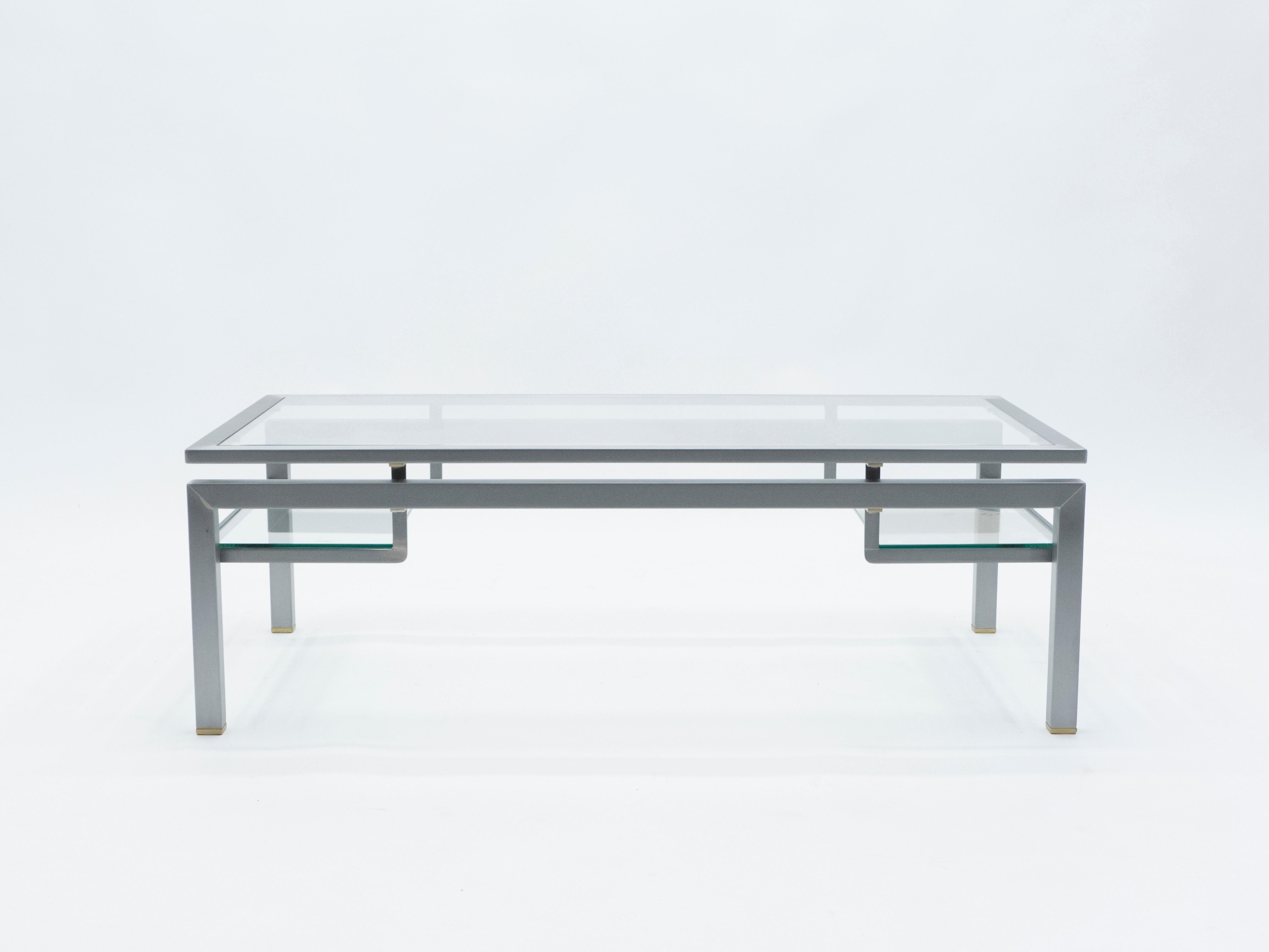Simple lines point to this coffee table’s mid-century roots. Designed by Guy Lefevre for Maison Jansen, it features silky brushed steel legs, two small glass shelves and a glass top. Its symmetry, elevated glass, and asian inspired and strong