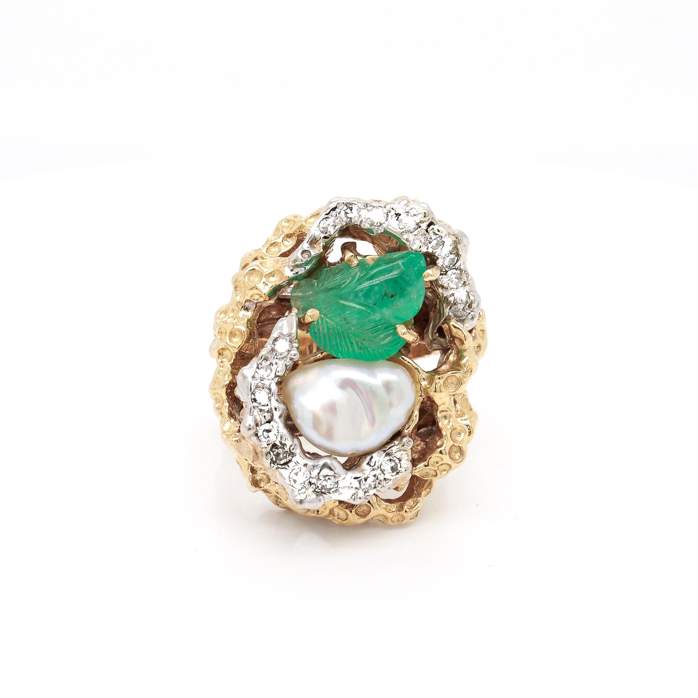 A fine signed Brutalist cocktail ring.

In 14 karat yellow gold.

Centered on a baroque, freshwater pearl and a prong-set carved emerald surrounded by 19 small round cut diamonds set in white gold near-halo atop an openwork high-set Brutalist gold