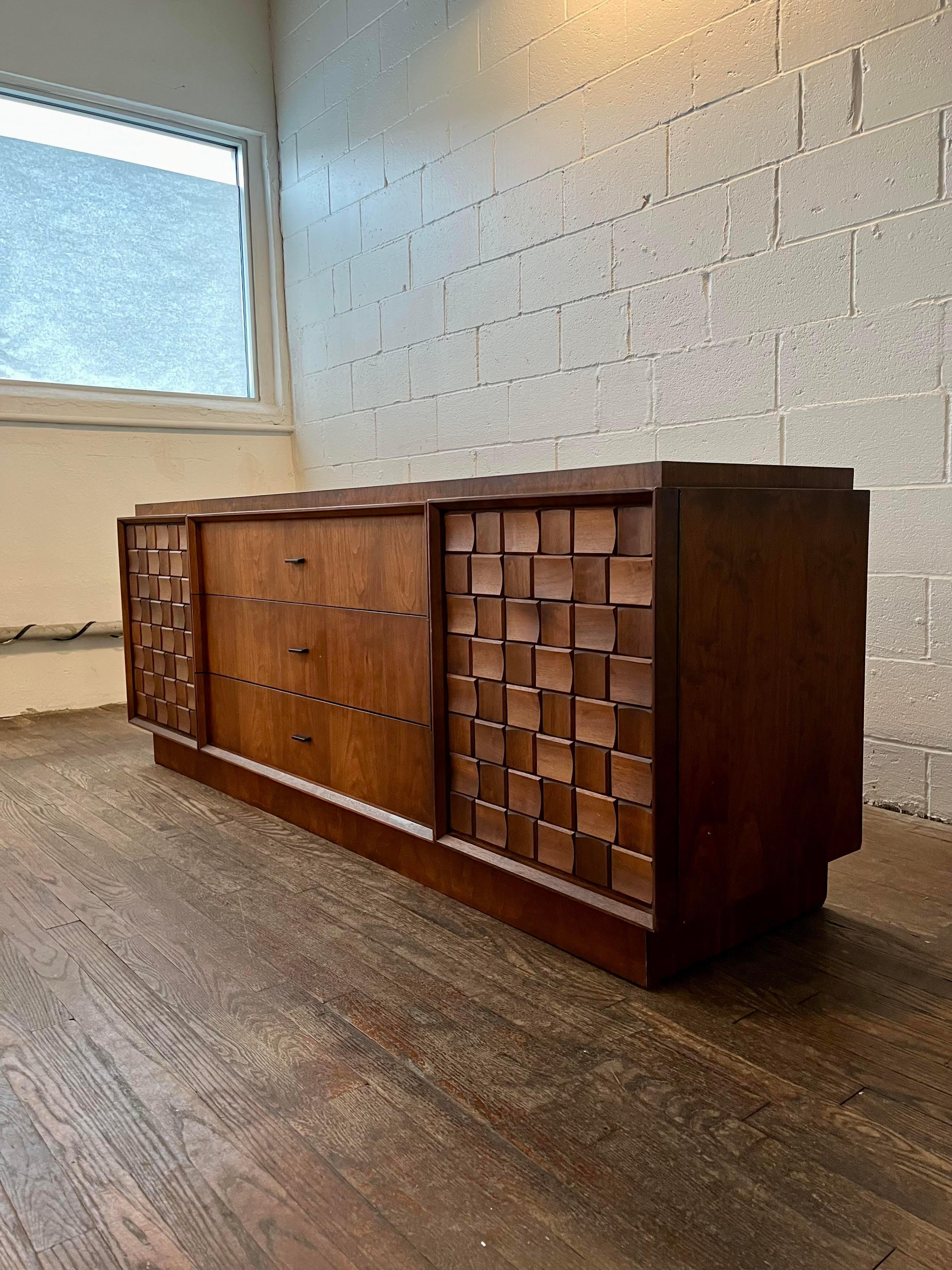Spectacular brutalist-style, 9-drawer, low dresser. It has three long drawers in the center with additional smaller drawers behind each of the two doors. The entire piece is finished in gorgeous walnut. The doors are covered in solid walnut blocks