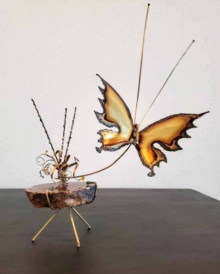 A signed Brutalist mixed metal sculpture from the mid-20th century, delicate miniature size, having finely detailed sculptural cut metal butterfly, flying above abstract flower and foliate form twisted scroll ribbon gilt brass strips, attached to a