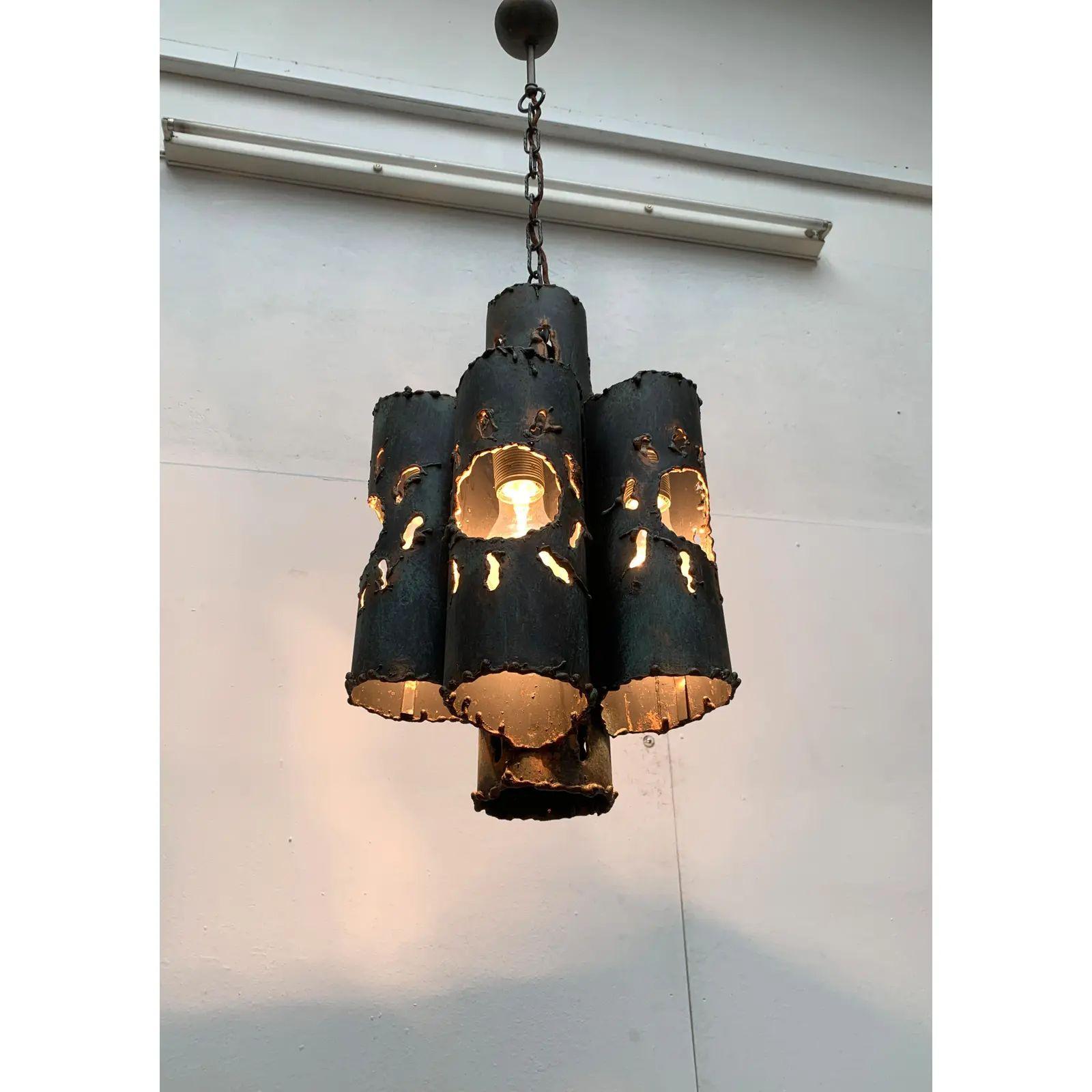 Lampadario in acciaio dal design brutalista.

Il lampadario è composto da tubi d'acciaio di diverse altezze, disposti radialmente intorno a un nucleo centrale. I tubi sono dotati di ampie aperture realizzate con una torcia da taglio. I bordi e gli