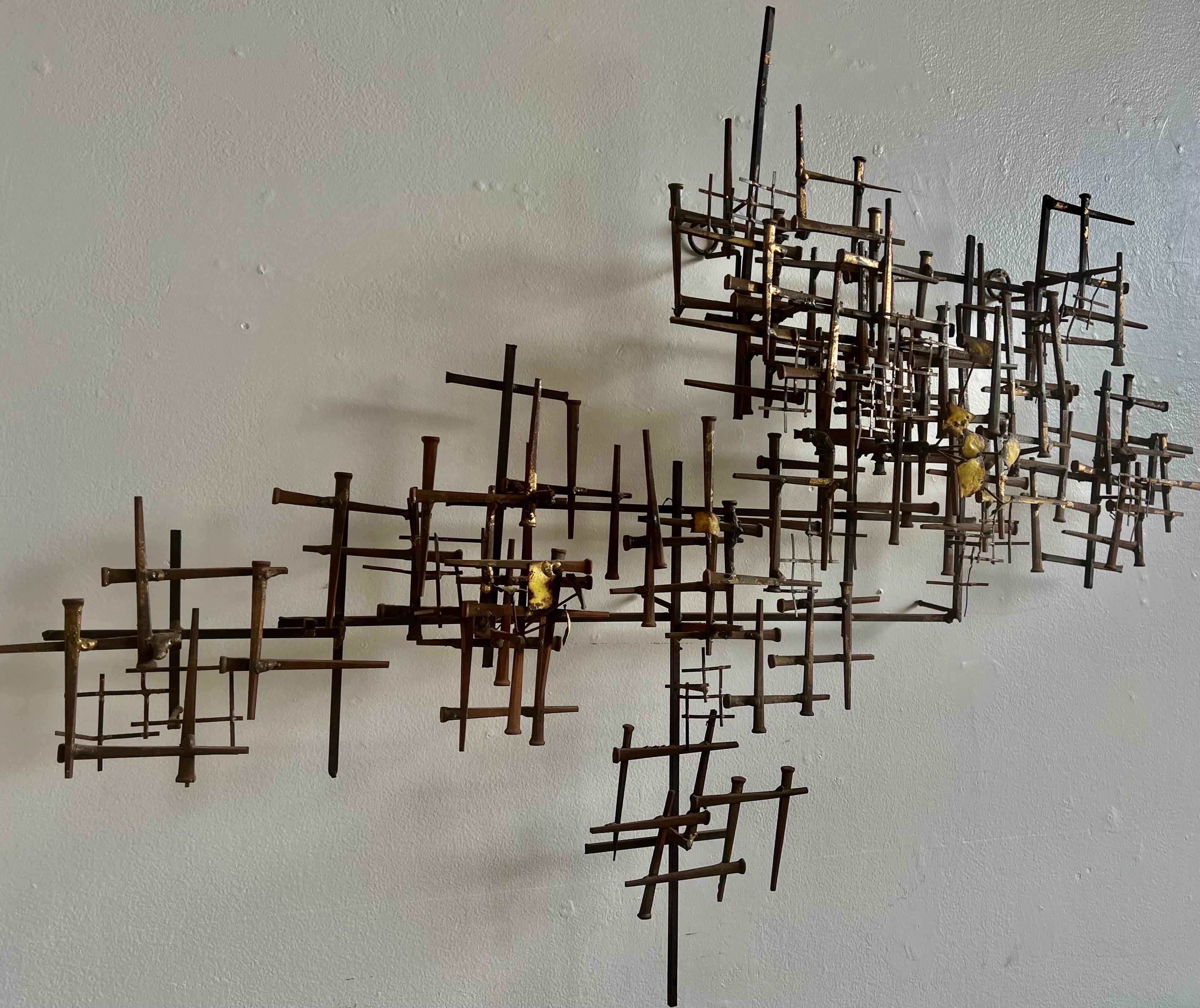 Prime example of Brutalist nail wall art.
This is a multi layered mixed media piece made of iron and brass with gold leaf accents.
The oxidized metal nails are soldered decoratively.  


