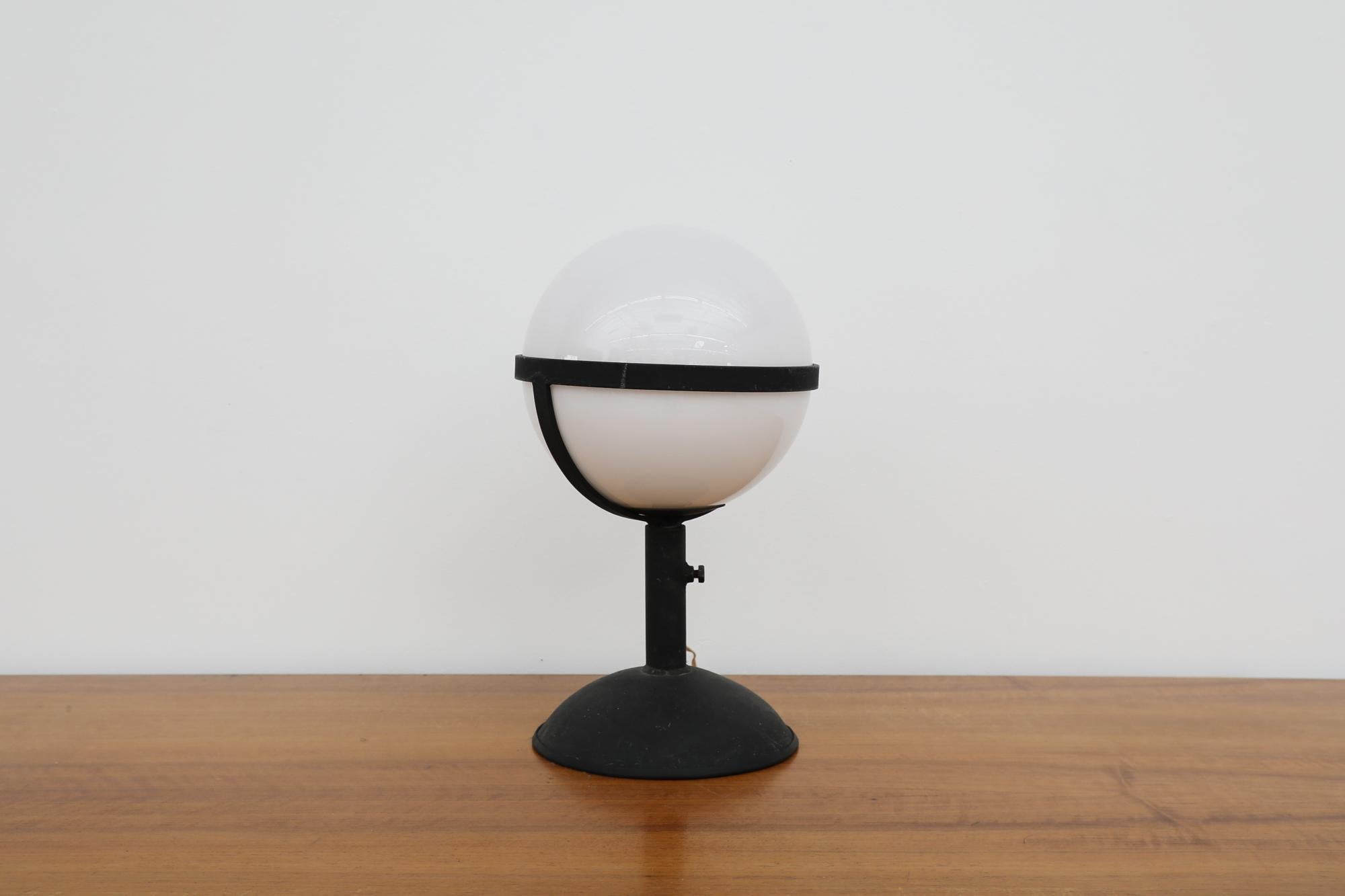Brutalist table lamp with heavy steel pedestal base and delicate blown opaline globe shade. In original condition with visible wear consistent with its age and use.