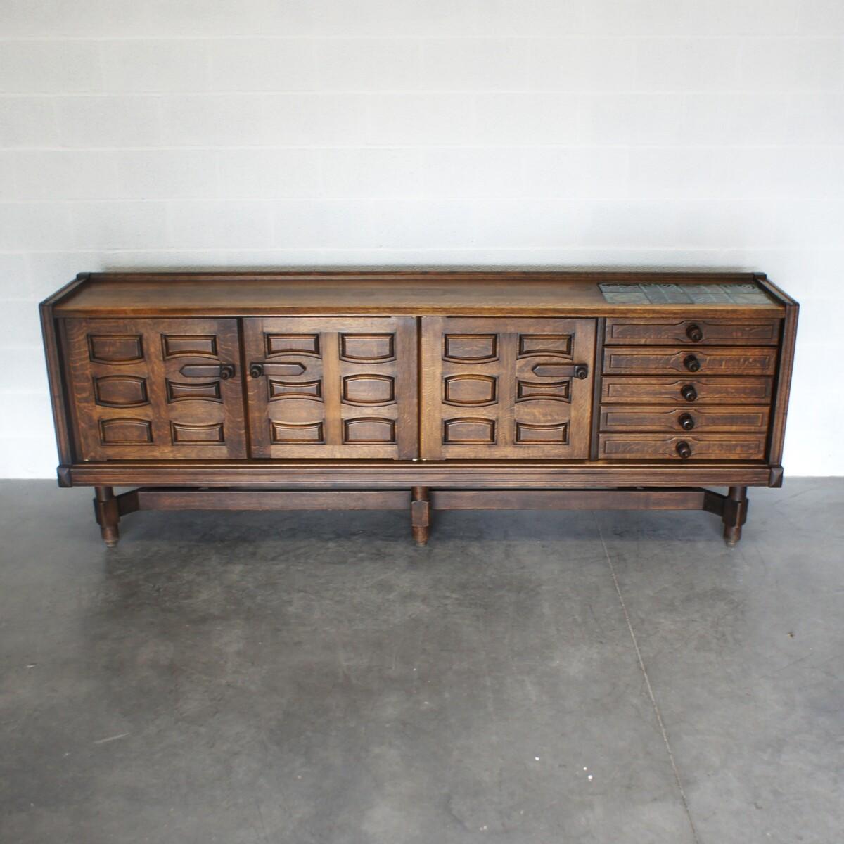 Large brutalist sideboard in waxed oak, designed by Guillerme et Chambron. Composed of four swing doors opening on vast storage space, and four drawers among which a double one on the side. The tray is adorned with eight ceramic tiles made by