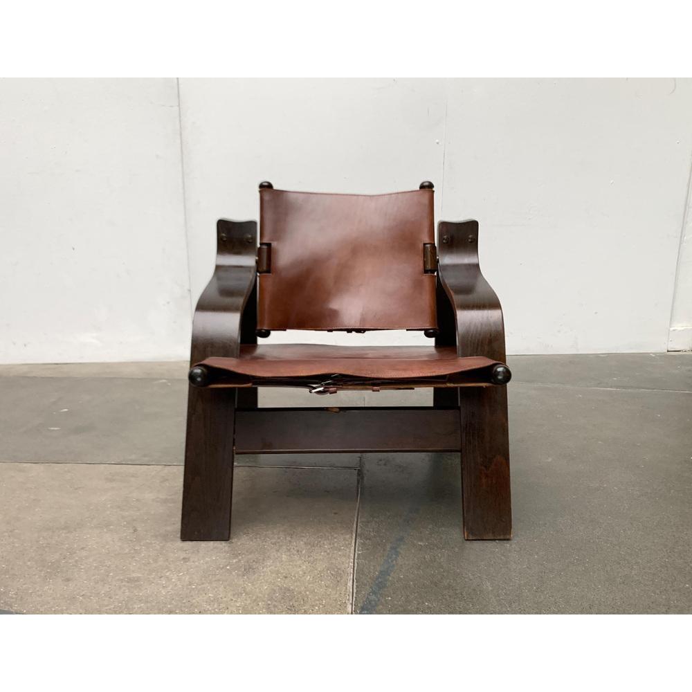 Imposant armchair with leather covering.

A brutalist design. An impressive and cozy solitaire. The material combination of dark stained wood and brown leather is striking. The cheeks of the frame are made of curved plywood and screwed at the top.