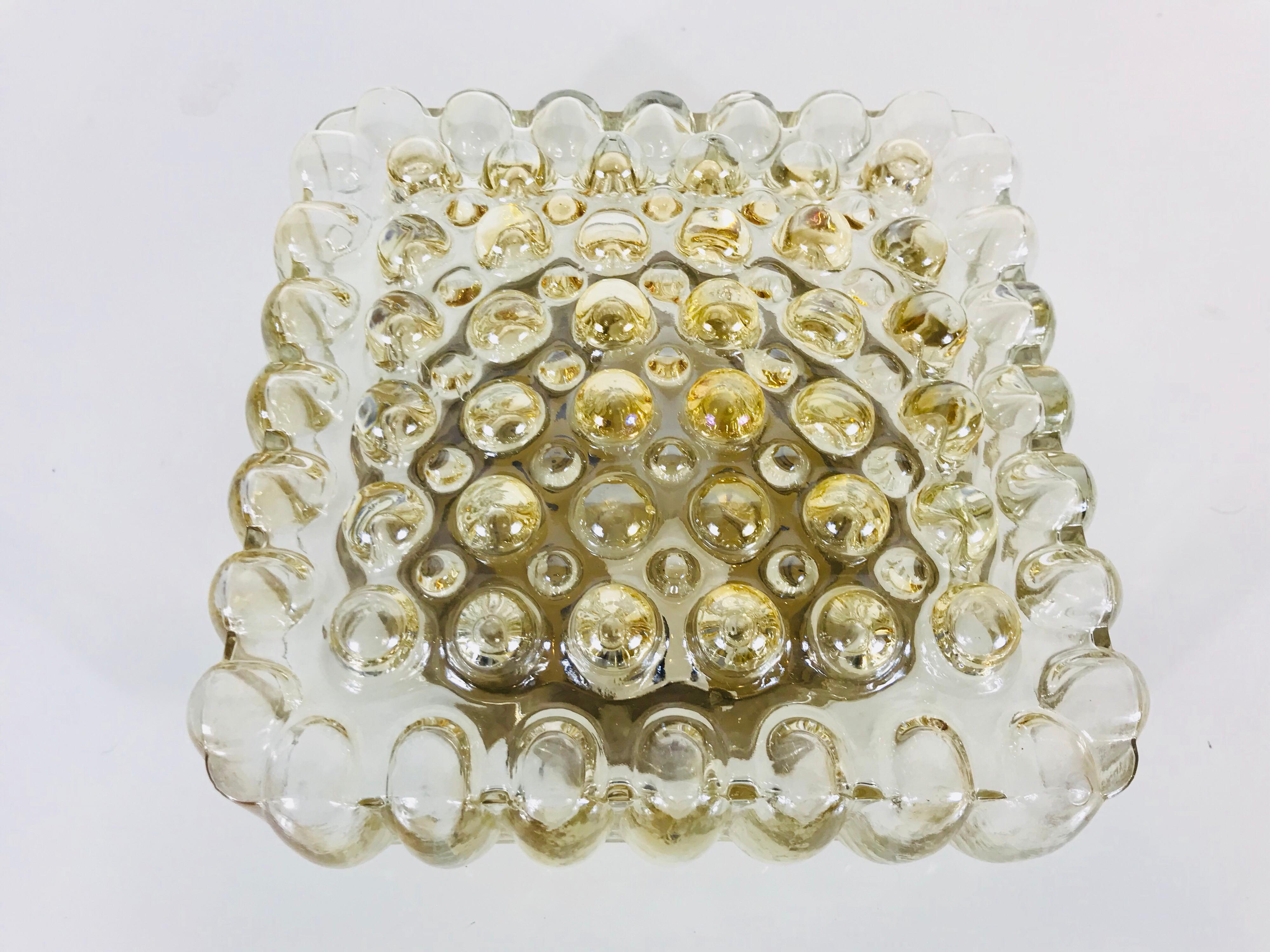 A bubble glass flush mount by Limburg made in Germany in the 1960s. The amber bubble glass is a design by Helena Tynell. The light has a square base made of brass.

Measurements:

Height: 10 cm

Diameter: 24 cm.
 
