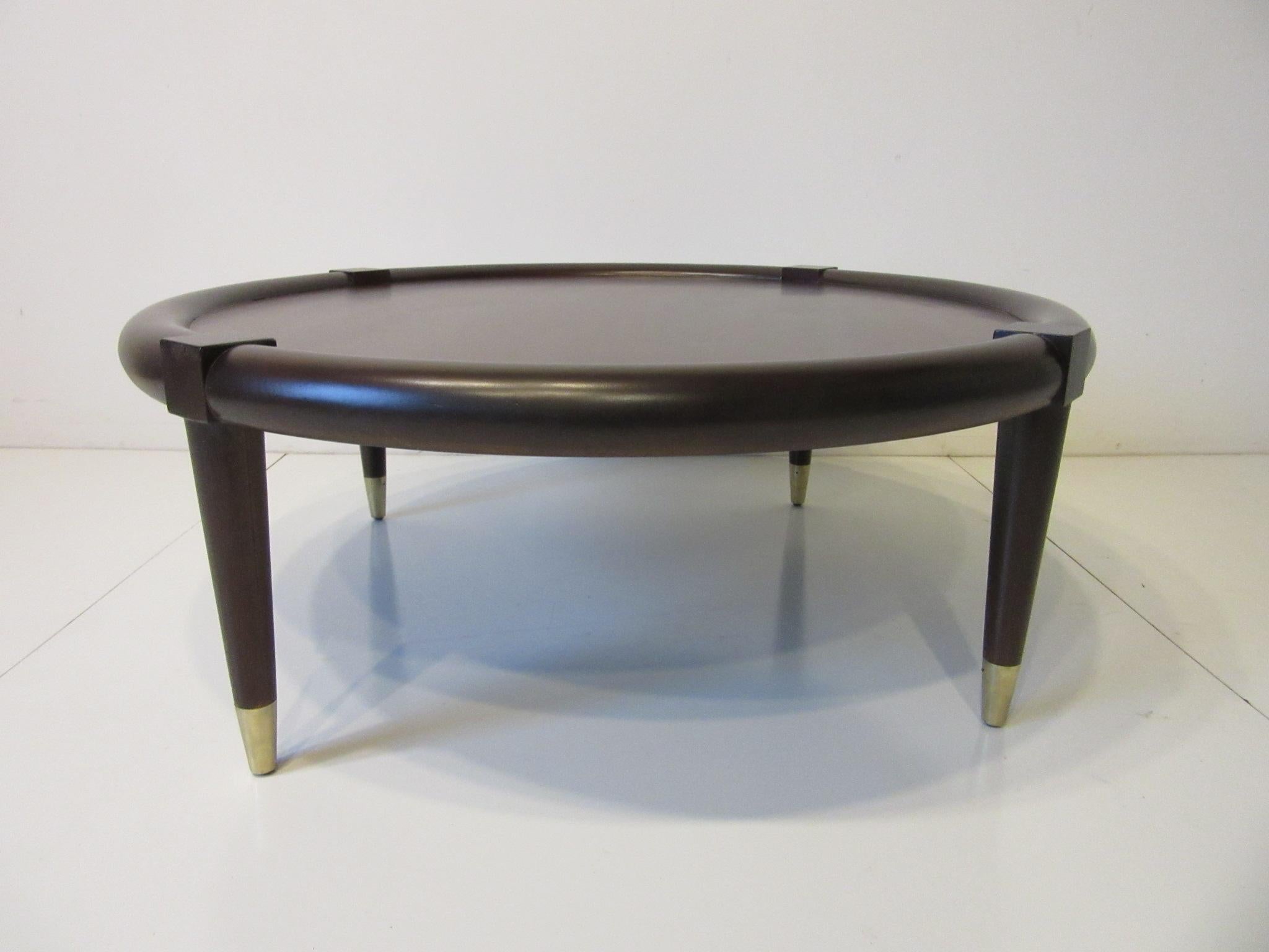 A round midcentury ebony toned bull nose coffee table with conical legs having brass tipped lower capped feet. The inserted wood center is very well grained and toned a bit lighter giving the piece some depth and can work in many different interiors