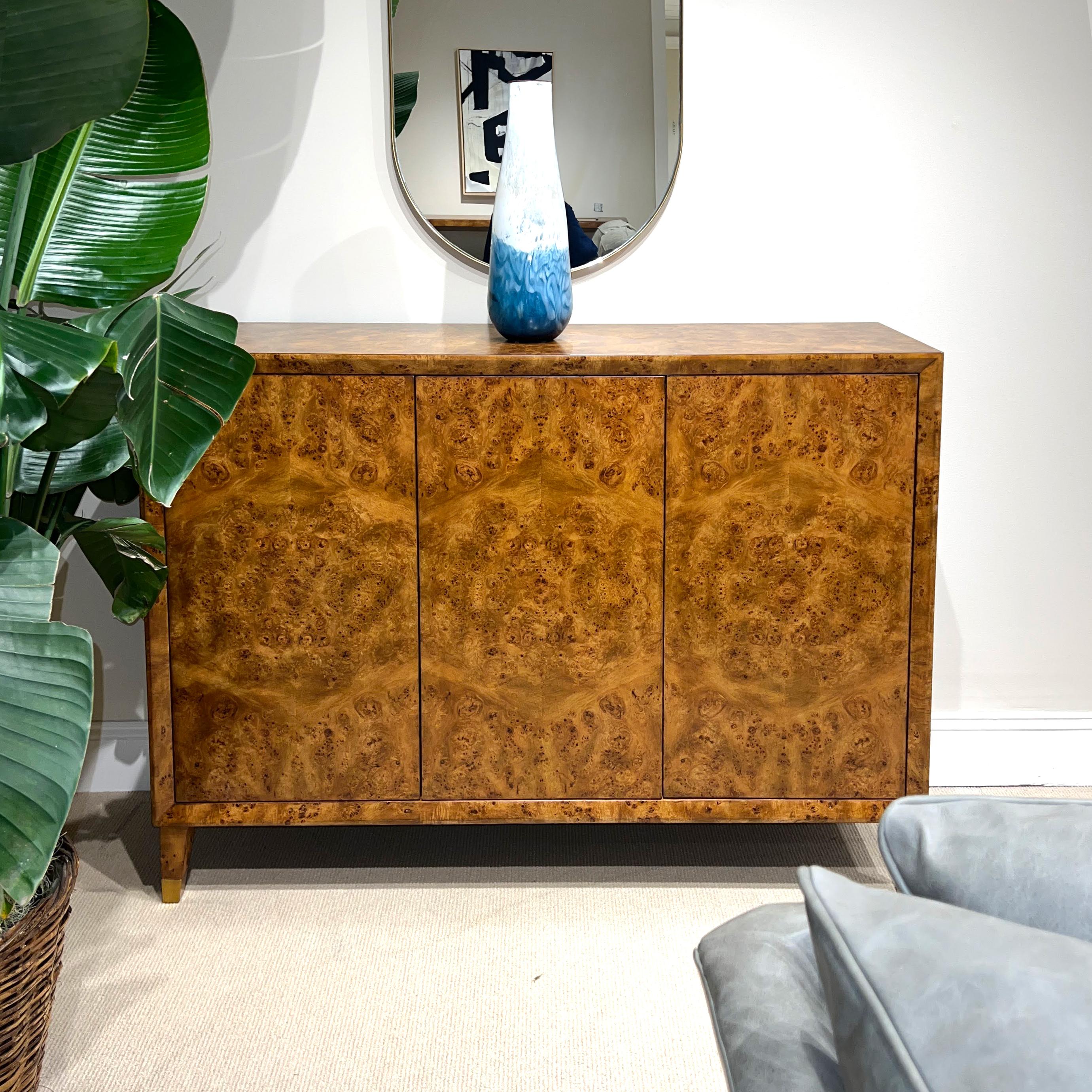 Midcentury Burl Credenza. This tall narrow three-door sideboard credenza has a warm 'rustic' hand-rubbed mappa burl veneer, a beveled frame surrounding the doors, an interior fitted with shelving, and raised on square tapered and flared