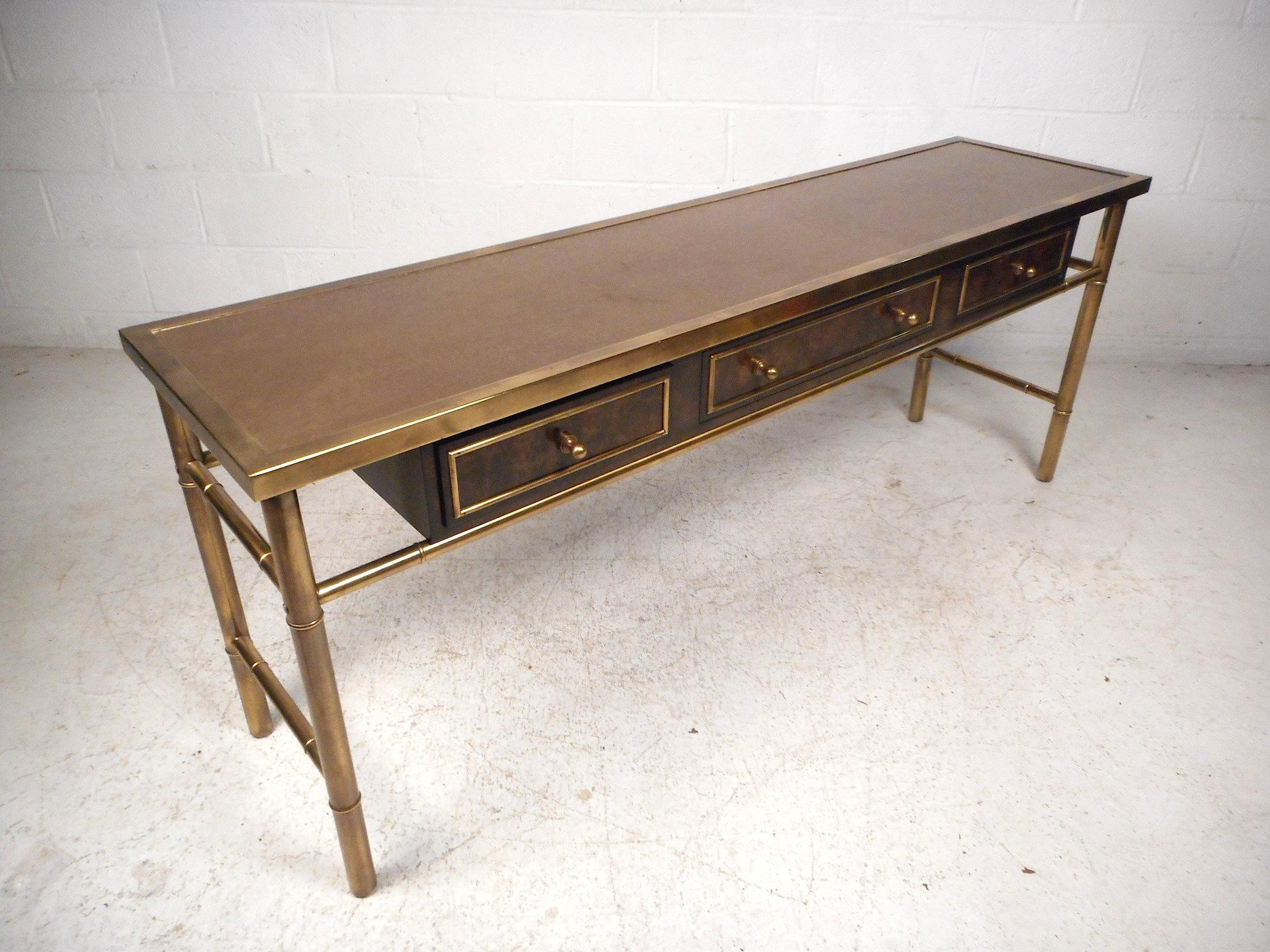 Impressive midcentury brass console table by Mastercraft. Three drawers for storage with finished burl wood fronts. Brass frame and siding with an etched top. Sure to make a great addition to any home, business, or office's modern interior. Please