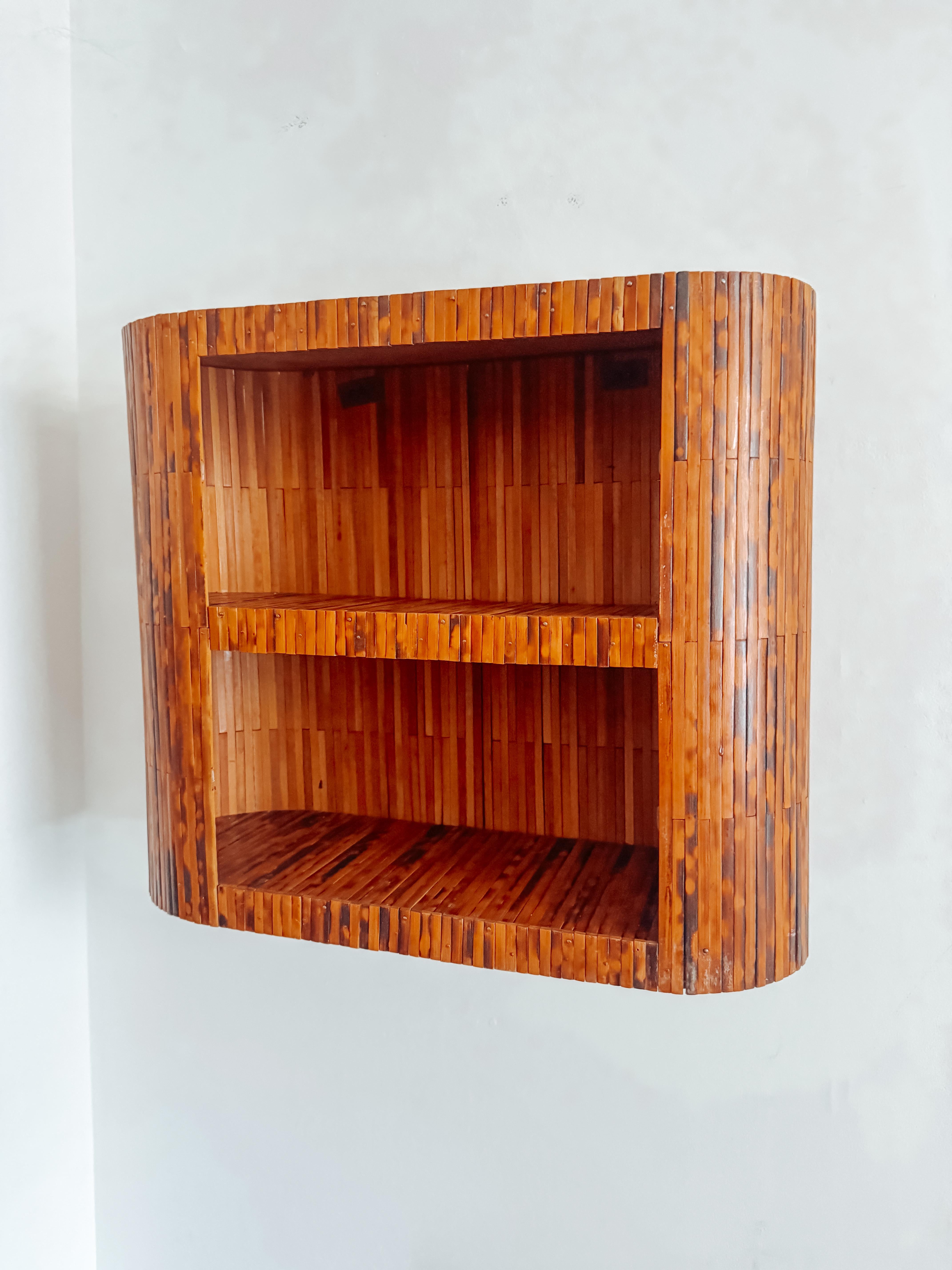 Uno splendido scaffale da parete in stile Mid-Century Modern realizzato con canne di bambù bruciate, risalente agli anni '60. Questo pezzo scultoreo presenta un telaio curvo e avvolgente con doghe verticali finemente dettagliate che creano un ritmo