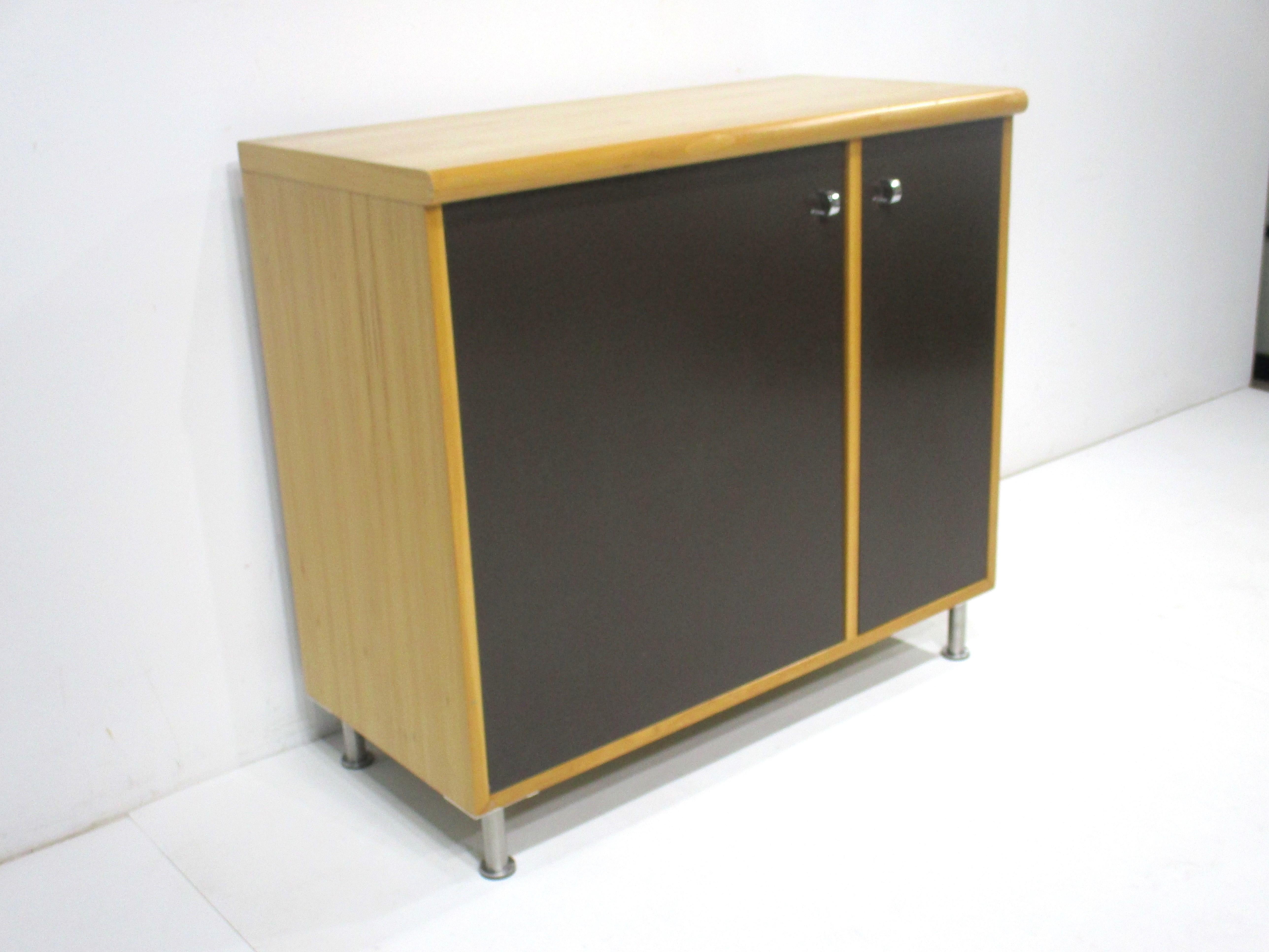 A two door smaller sized cabinet with birch wood case and dark chocolate doors having chromed U shaped finger pulls . Sitting on adjustable brushed stainless steel legs with foot pads to protect your floors . In side are matching birch adjustable