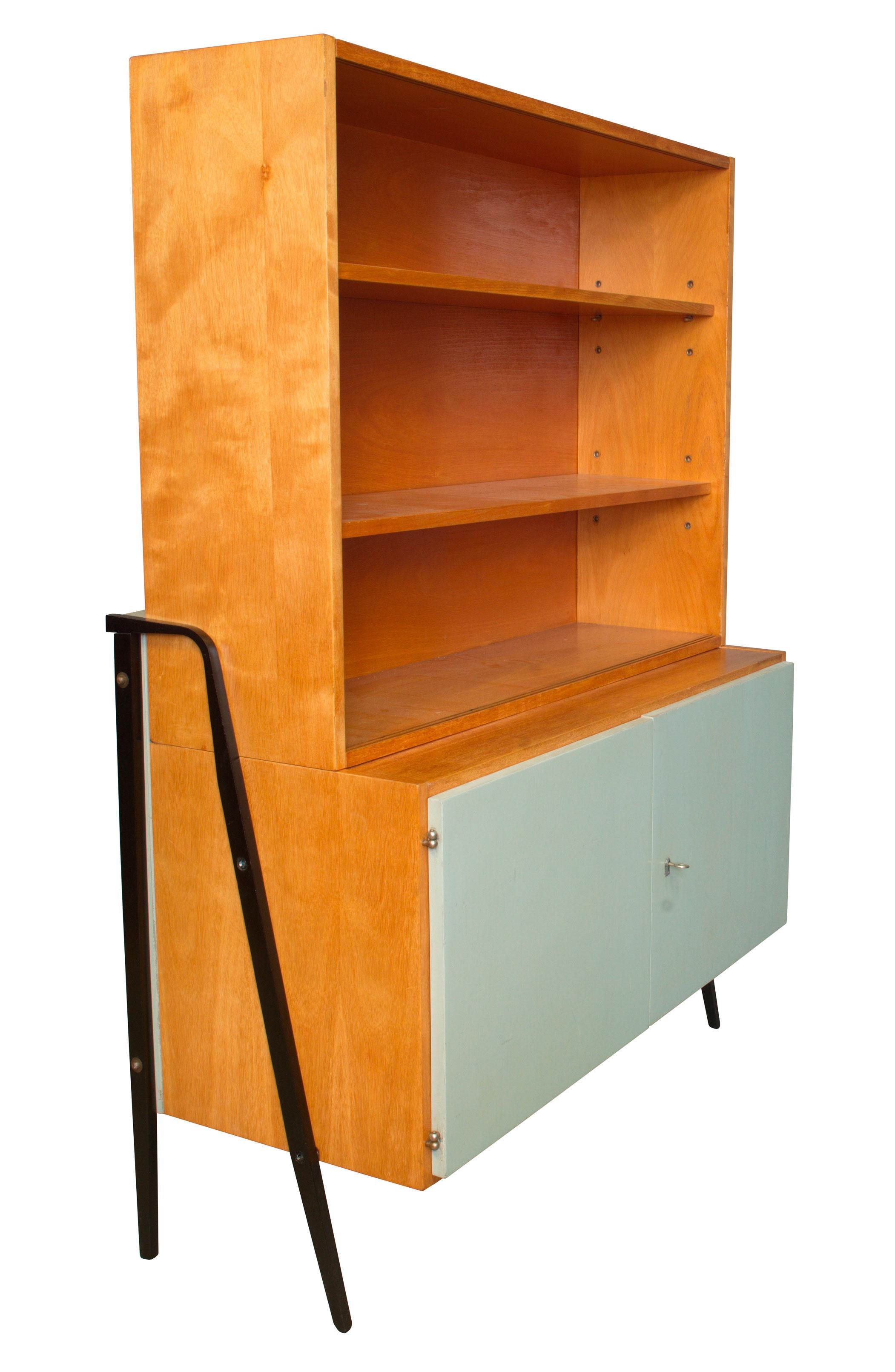 This Mid Century Cabinet has been designed and produced by UP Zavody in the 1960’s, in former Czechoslovakia. The cabinet is divided into two parts. The top part consists of open shelving protected by two sliding glass doors. The botom part has one