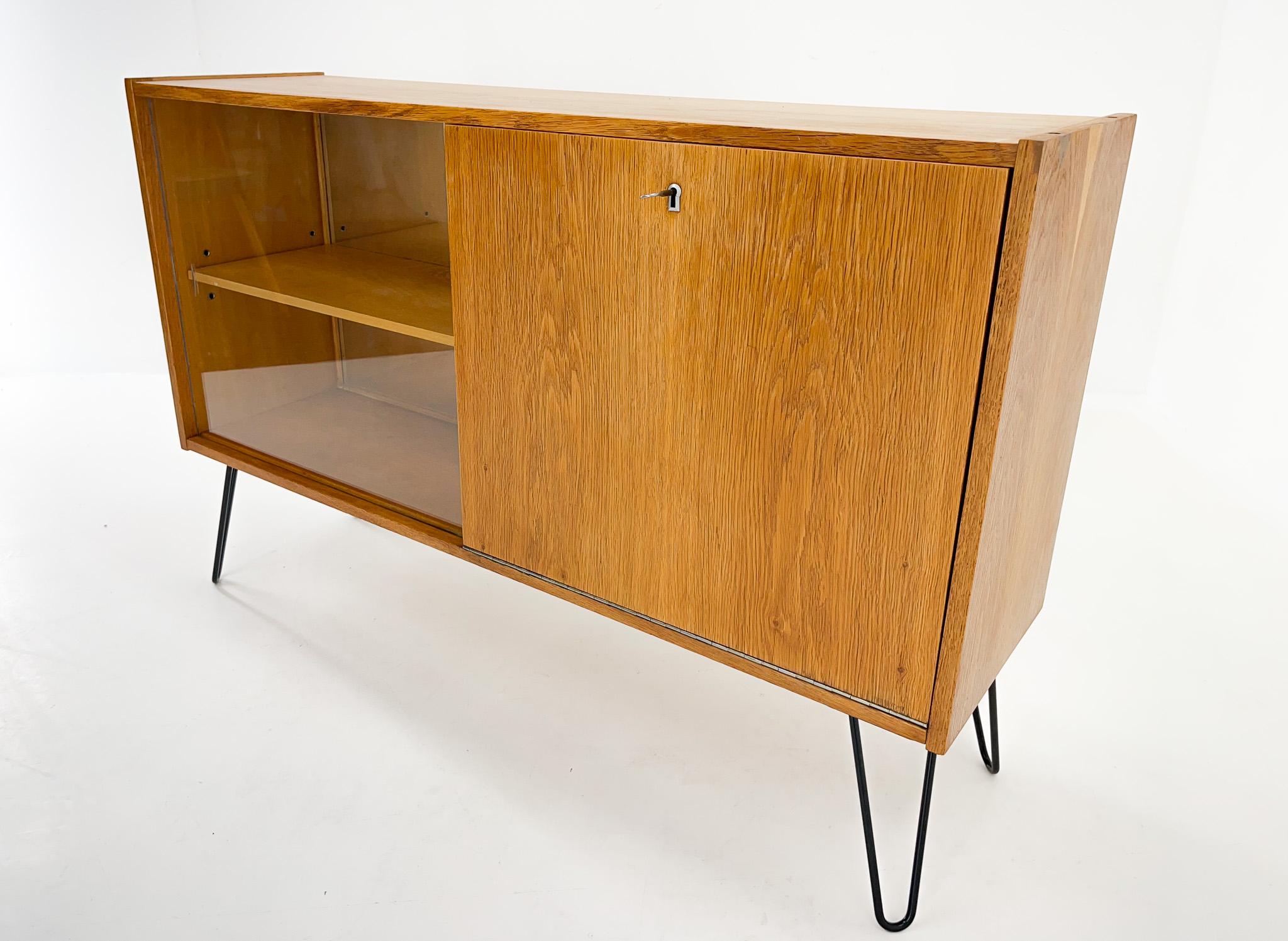 Vintage cabinet with a small bar on one side and a glass sliding door on the other. The part on the side of the glass door has a shelf and the back is mirrored. The cabinet is in original condition with new herpin legs. The key is original.