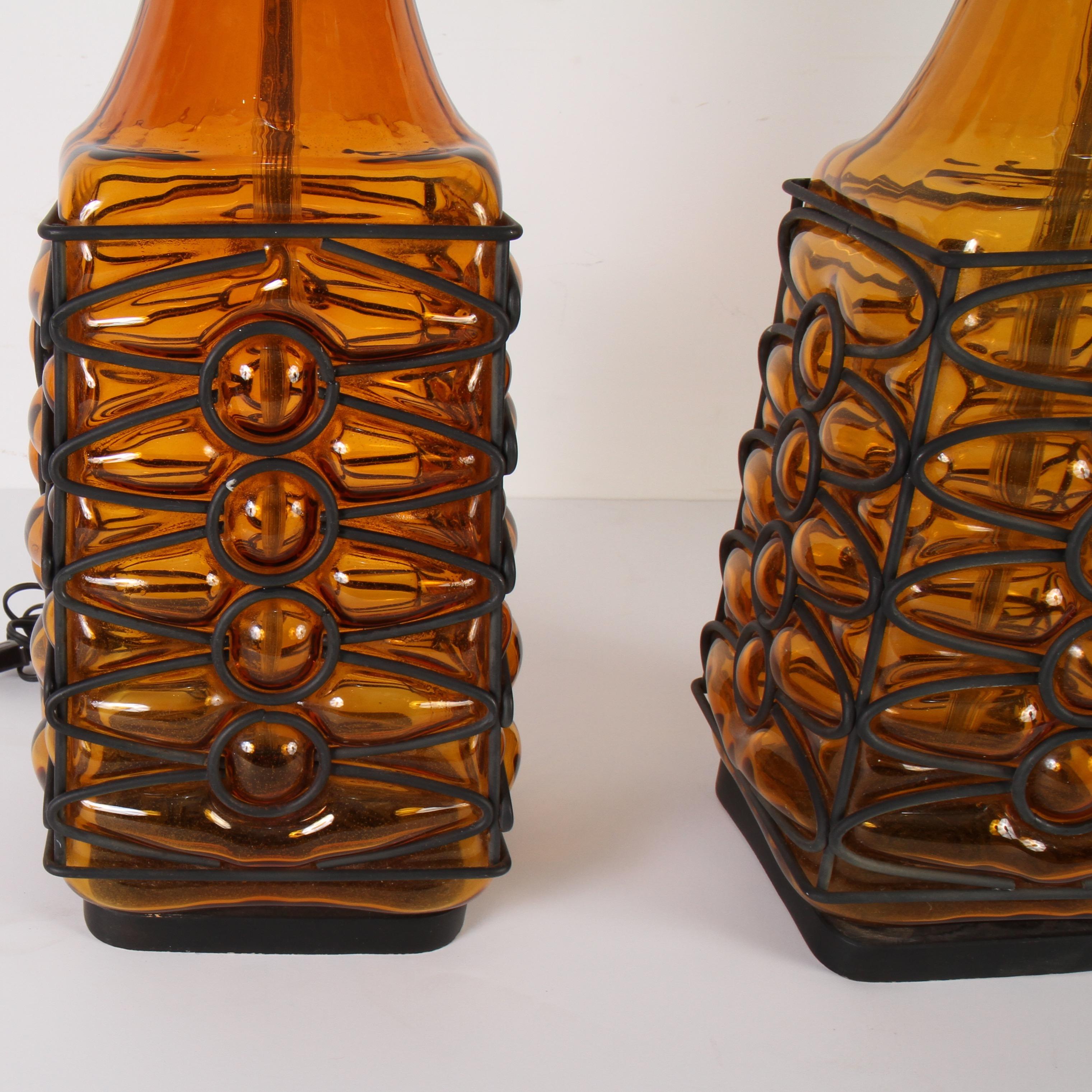 Artisans hand blow glass into a metal fretwork to create this lamp’s intriguing texture. The blackend metal provides a handsome contrast to the orange glass. These are most likely from the sixties or seventies.