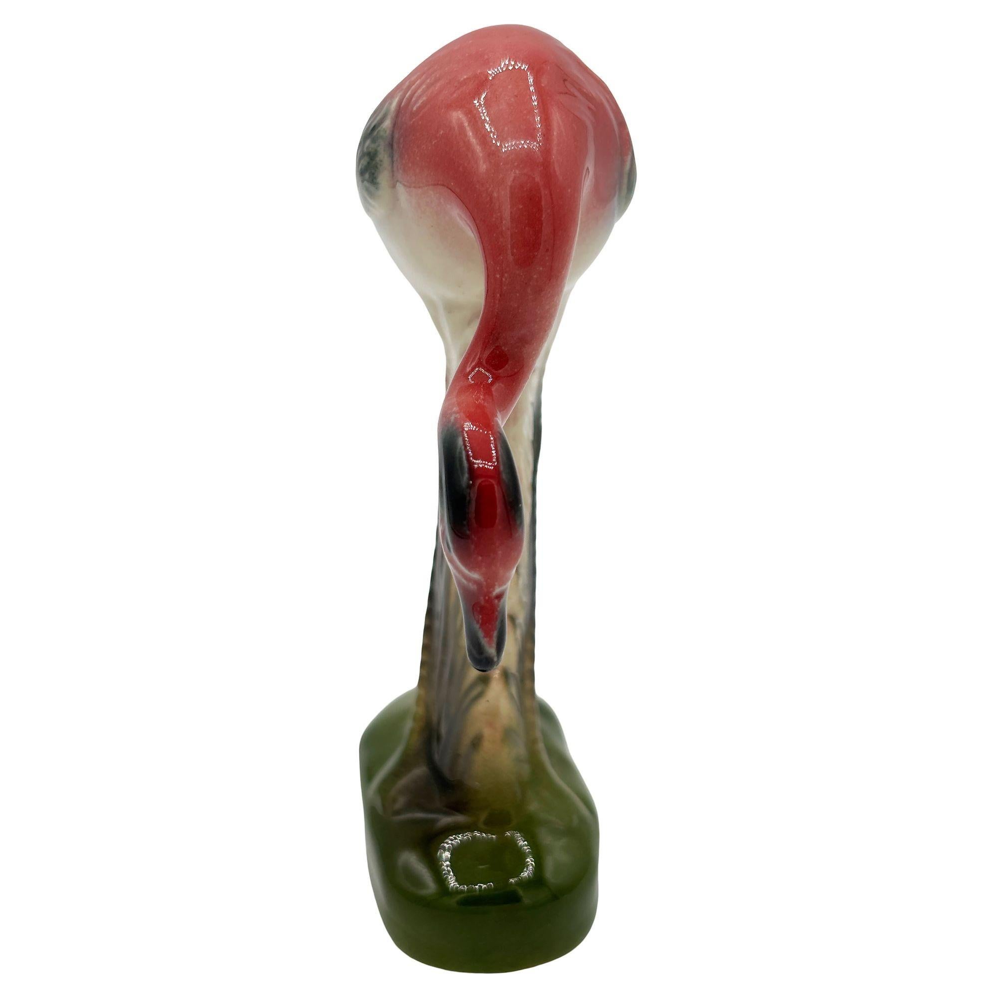 Mid-century pink and green drinking flamingo ceramic figurine. The statue detailed a pink flamingo with long legs, a slim, tall form standing on a grassy field, bowing down to take a drink. It comes in a gloss finish that highlights the rich pinks,