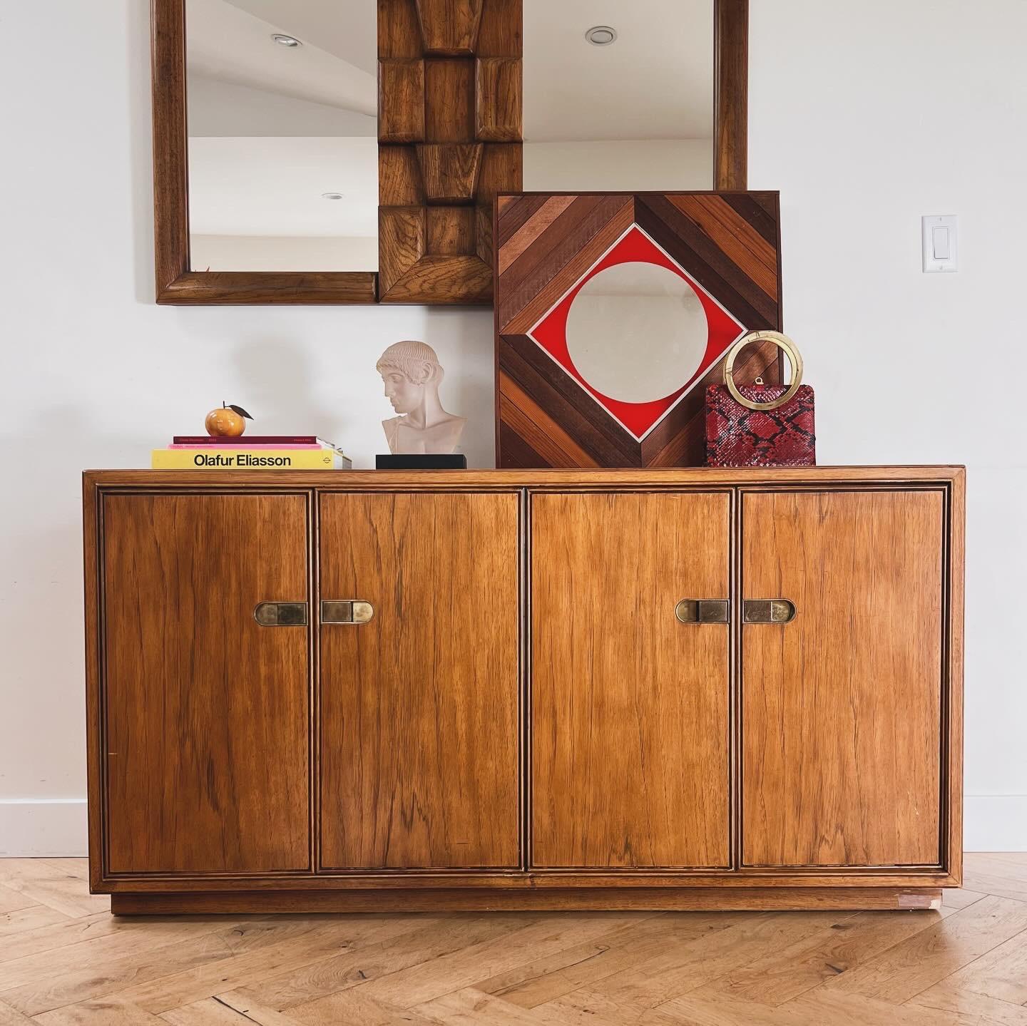  A mid century modern campaign sideboard / buffet / credenza in pecan wood with brass accents by Drexel Heritage Furnishings, circa 1970. Featuring engraved framing along the edges of the facade doors, this piece showcases high mcm design