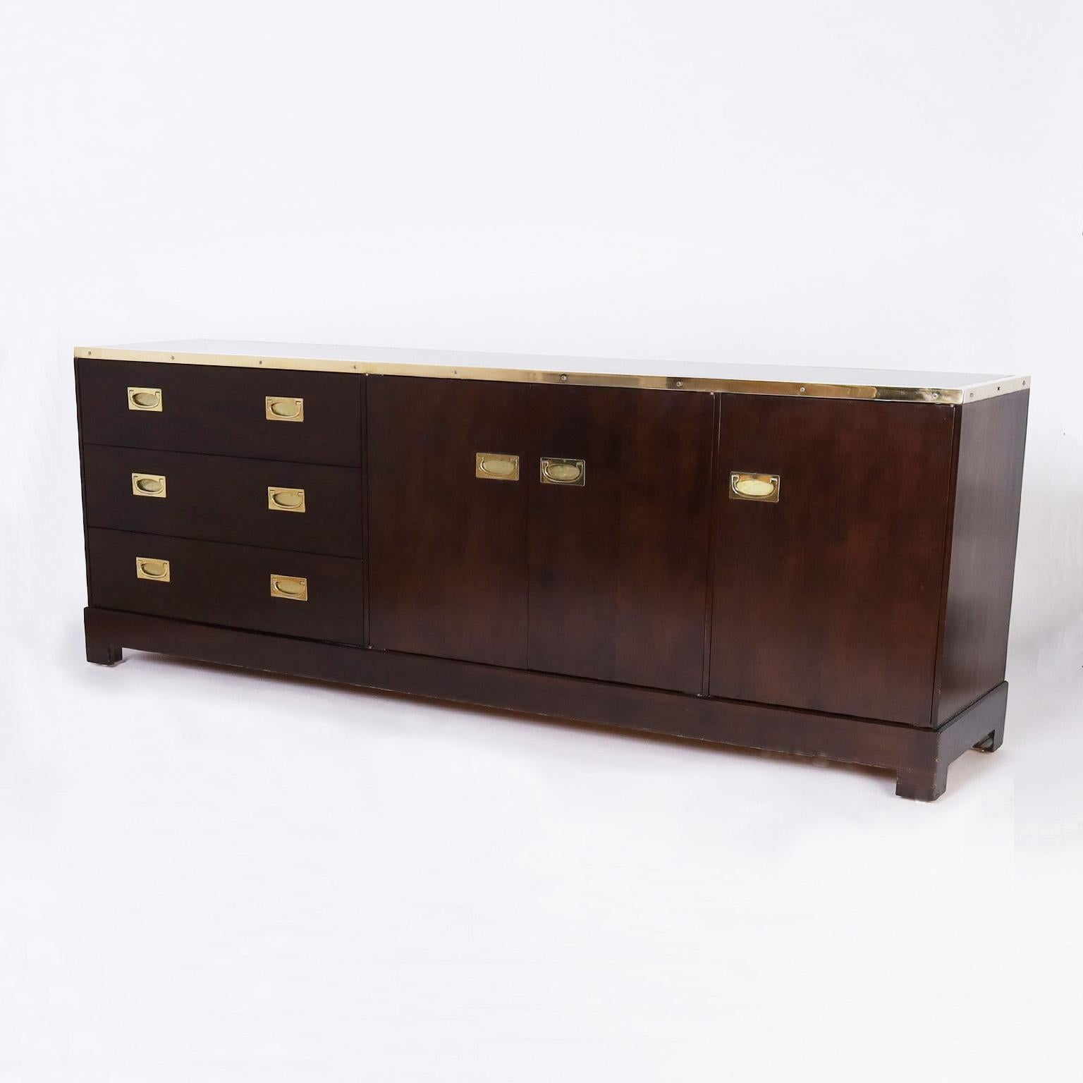 Chic mid-century chest or cabinet crafted in mahogany featuring multiple components including brass campaign style hardware including three drawers and three doors. Plenty of storage with a sleek modern form and stylized bracket feet. Signed