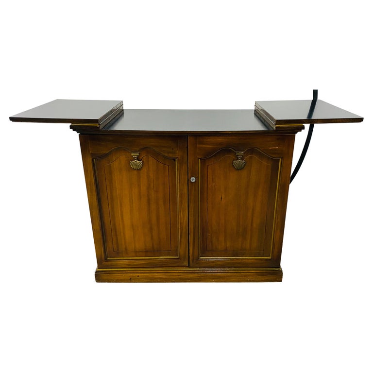 A stylish mid-century campaign style rolling dry bar cabinet server or chest. The functional and mobile dry bar or cabinet server has two unfolding extensions, converting to a serving bar with a painted black top and standing on wheels so it can be
