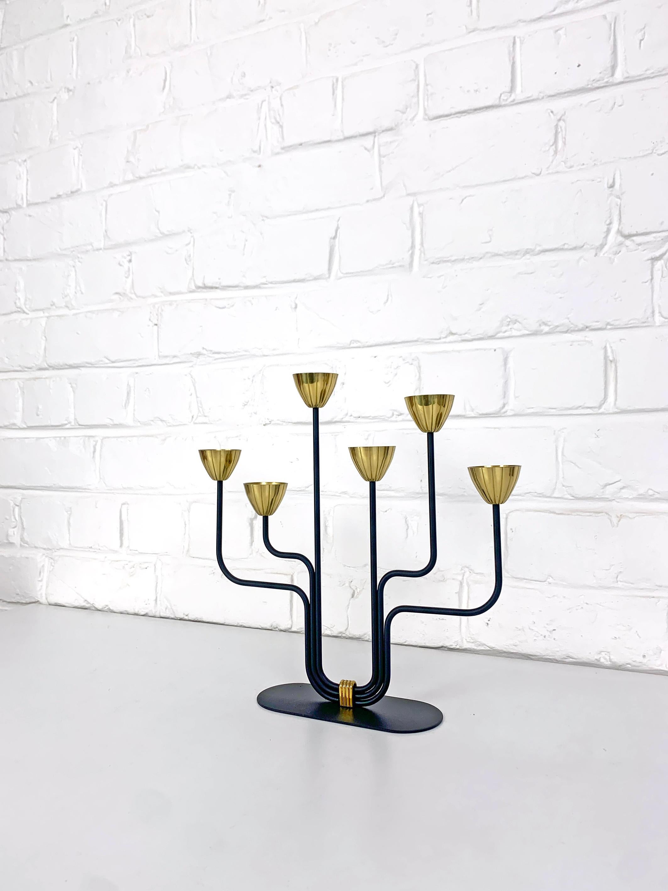 Swedish Modernist candle holder by Gunnar Ander. Produced by Ystad-Metall, located in the town of Ystad in Sweden. 

Stylised flowers in brass on 6 asymmetrical black enameled steel arms. This is the smaller model.

Both are signed with the Ystad