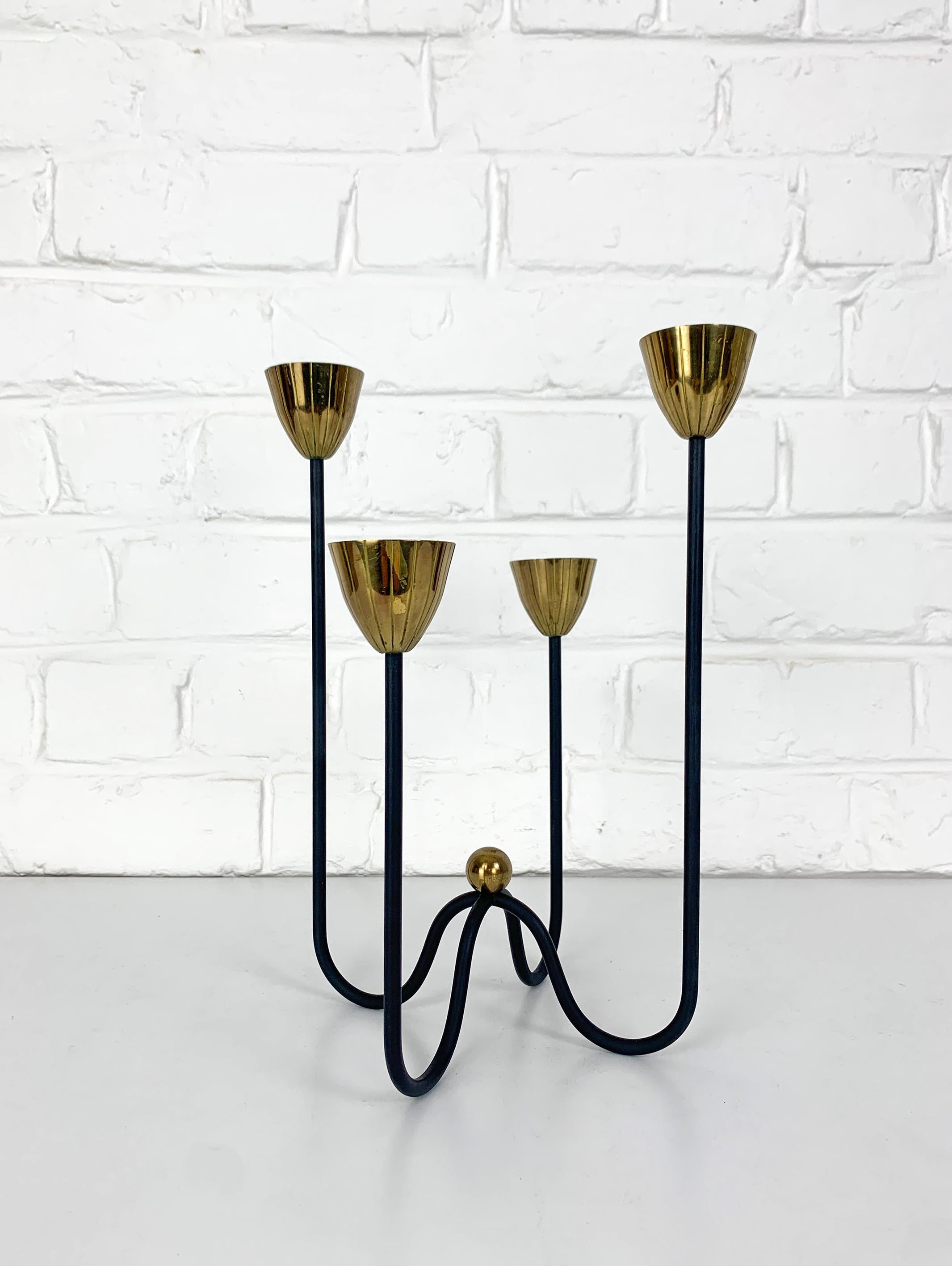 Swedish Modernist candle holder by Gunnar Ander. Produced by Ystad-Metall, located in the town of Ystad in Sweden. 

Stylised flowers in brass on 4 asymmetrical black enameled steel arms. 

Gunnar Ander is a Swedish artist born in 1908. He created