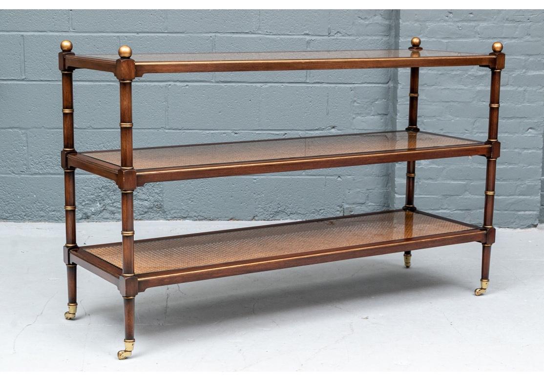 The mahogany frame with three glass covered inset cane tiers. The supports with gilt ring details and ball finials. Raised on brass casters.
Measures: Length 54