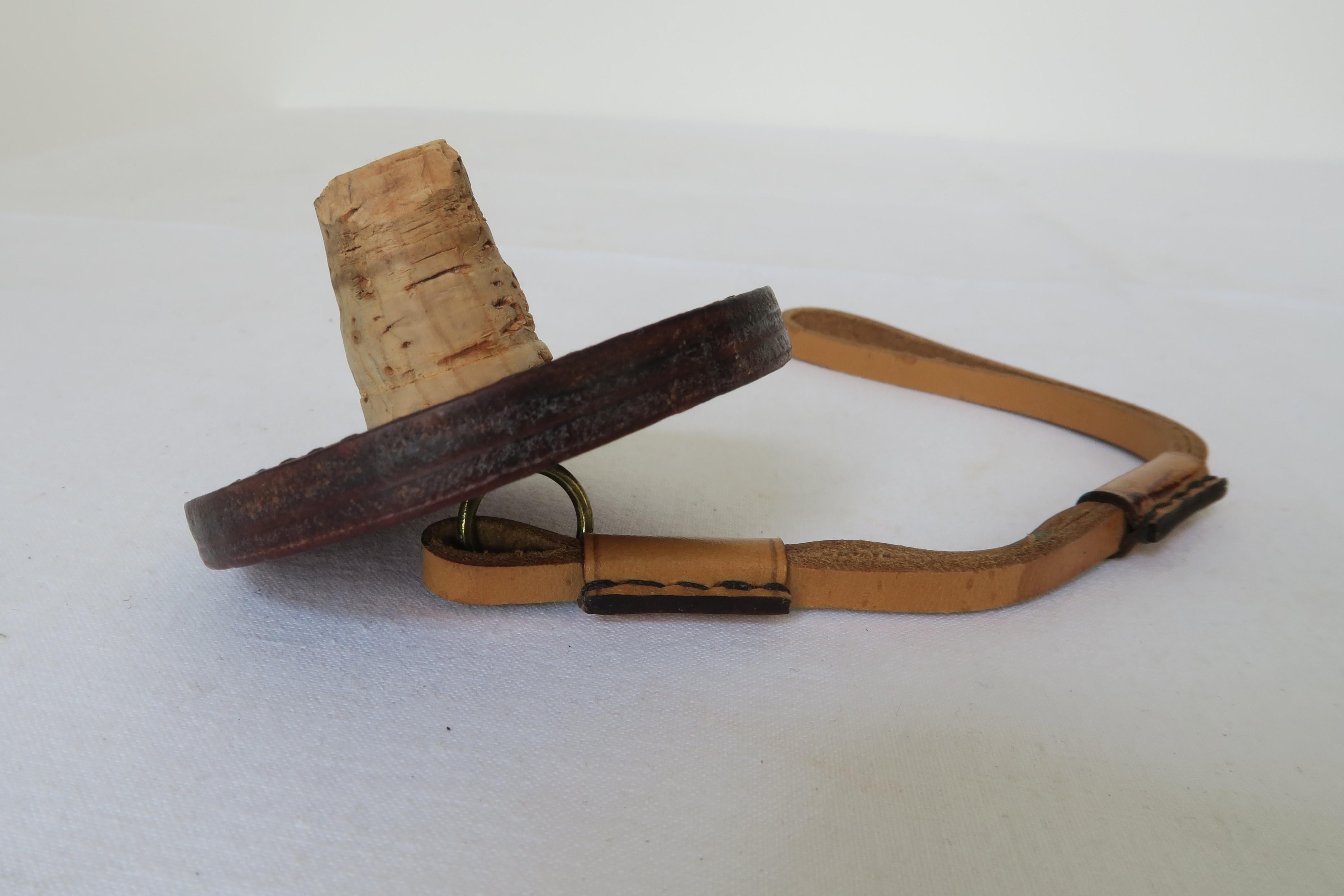 For sale is a unique piece of Mid-Century Modern design. The bottle stopper was carefully hand crafted out of leather. It has a brass eyelet connecting the round base of the cork to a 21.5cm long leather strap. It was produced in the renowned