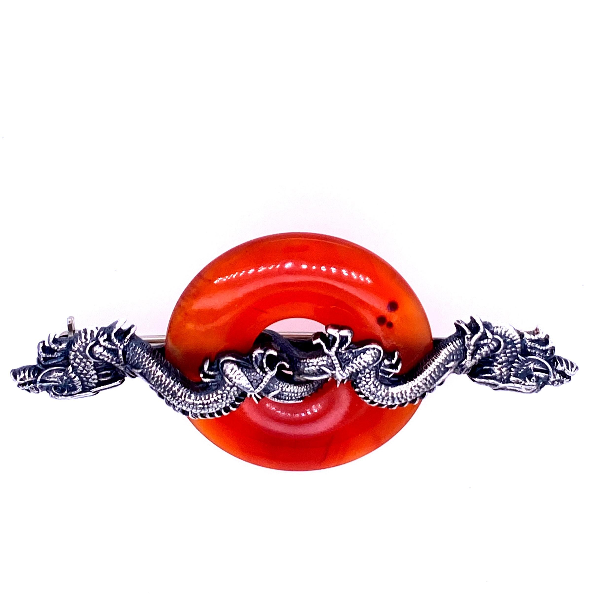 One sterling silver (engraved with AOSX) dragon pin by Carl Schon measuring 2.5 inches long x 1.25 inches wide featuring one 1.25 inches in diameter donut shaped carnelian with a tradition pin back. Circa 1950s