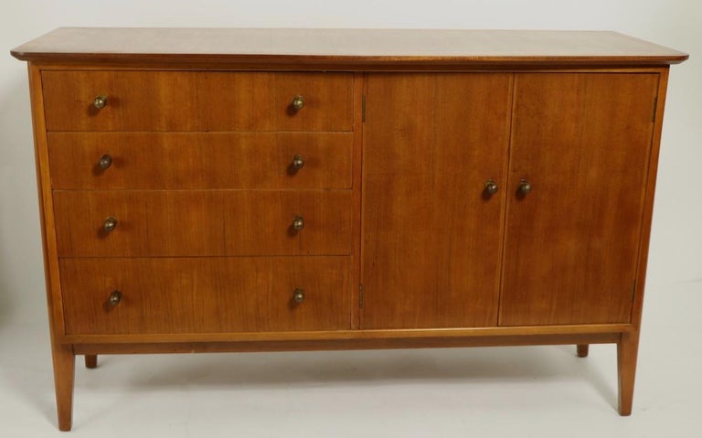 Chic and stylish server sideboard by noted English maker Gimson and Slater, as part of the Carousel line, retailed by Heals of London. The case has four drawers, each having cast brass pulls, flanked by two doors which open to reveal shelved