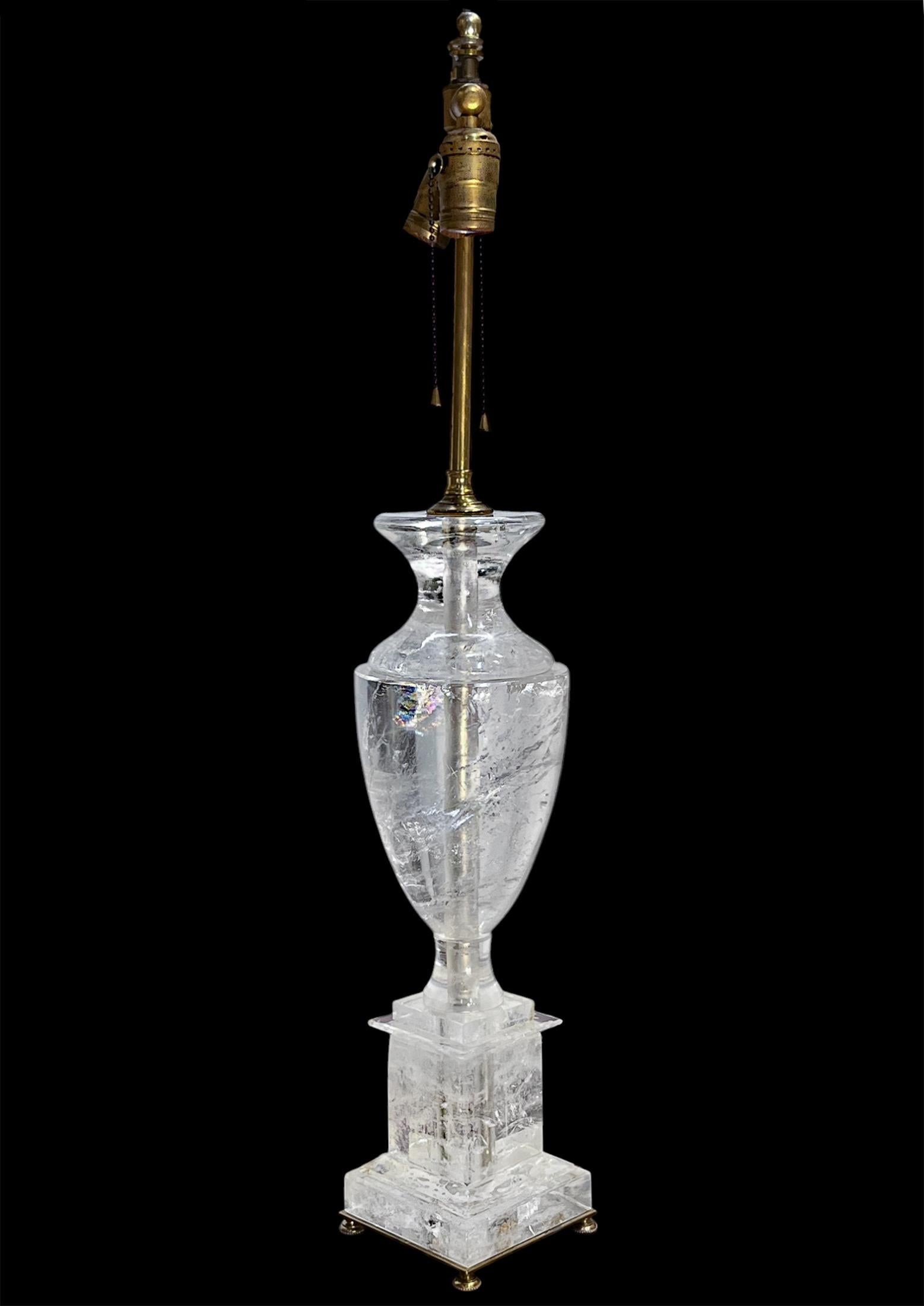 A large piece of rock crystal carved into a vase and mounted as a table lamp on a cut rock crystal base. The smooth polished edge of the vase highlighting unique, large, inclusions within the stone that catch and reflect in the light