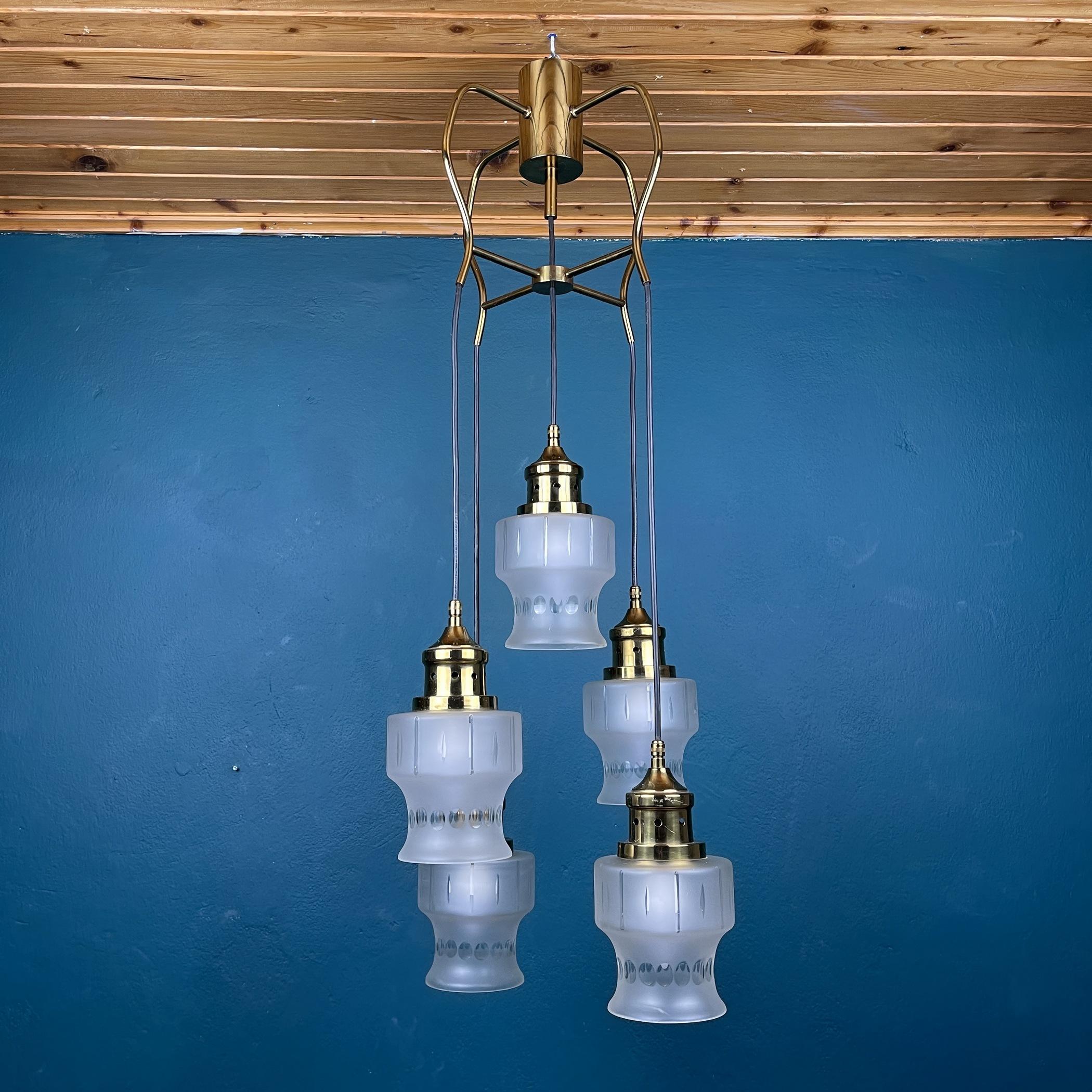 The rare Mid-Century Modern five-light cascading pendant lamp made in Italy in the 1970s. The lamp is made of a brass cross with five cascading glass lampshades. Plafond are made of heavy, thick glass with a relief pattern. Each pendant light