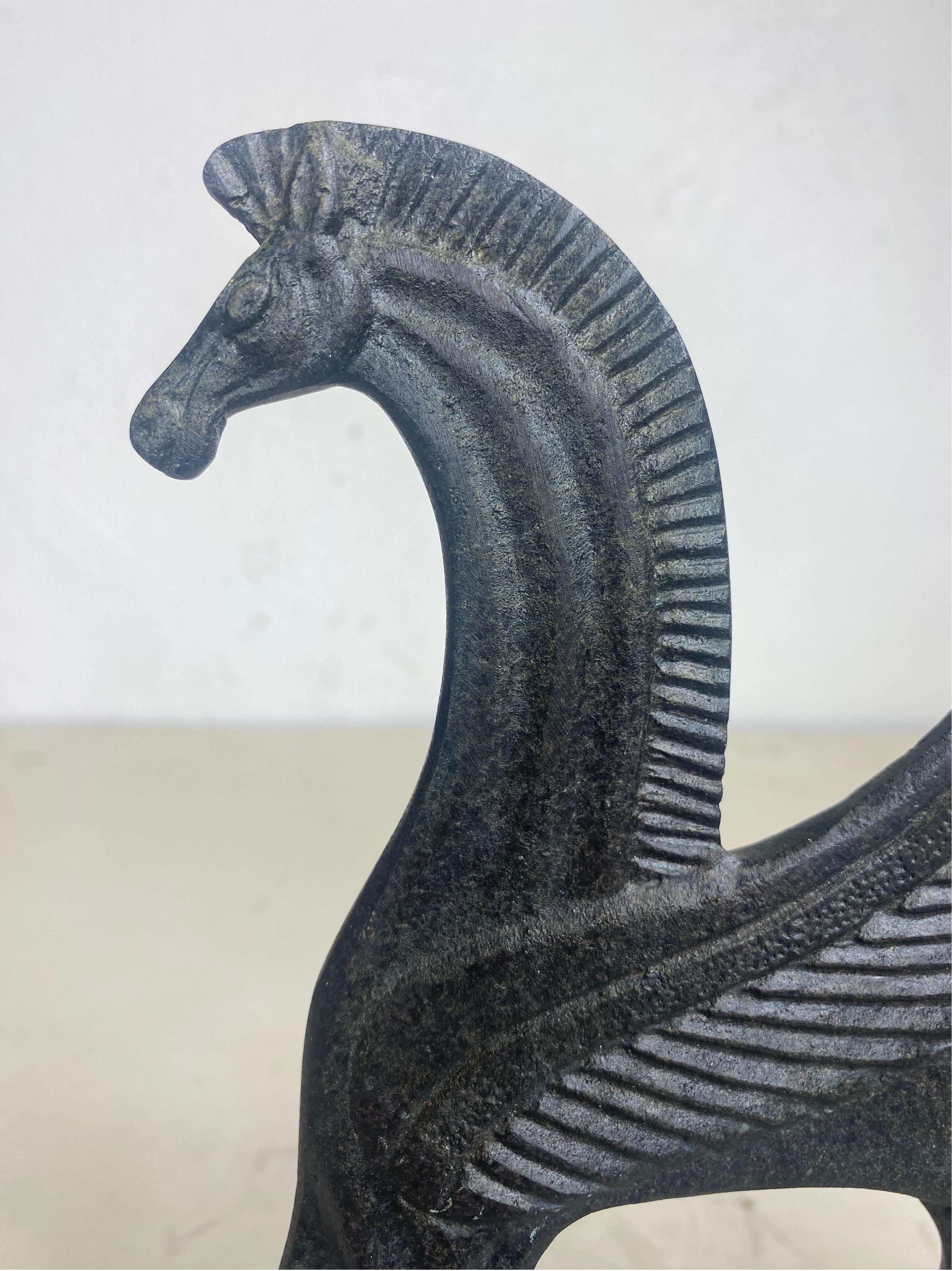 This is a mid century vintage cast iron sculpture of a mythical horse with wings and a figure. The sculpture has a dark bronze patina finish to the surface. The stylized horse has wings and the figure is carrying a spear. This piece is American made