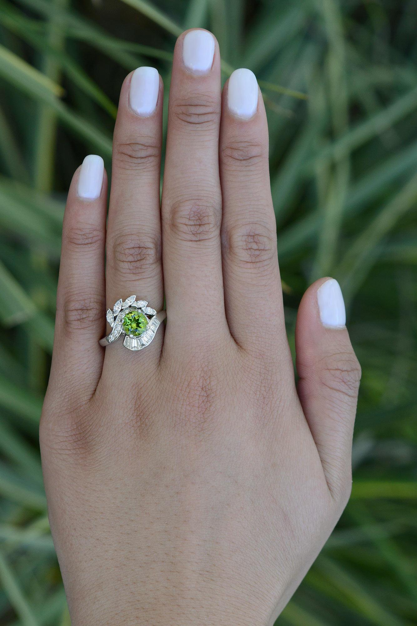 Your eyes have spotted a mid century peridot engagement ring, with an alluring design. The platinum setting is adorned with over a carat of sparkling diamonds, creating lush lashes, with a top quality gemstone peering out. A vintage gemstone bridal
