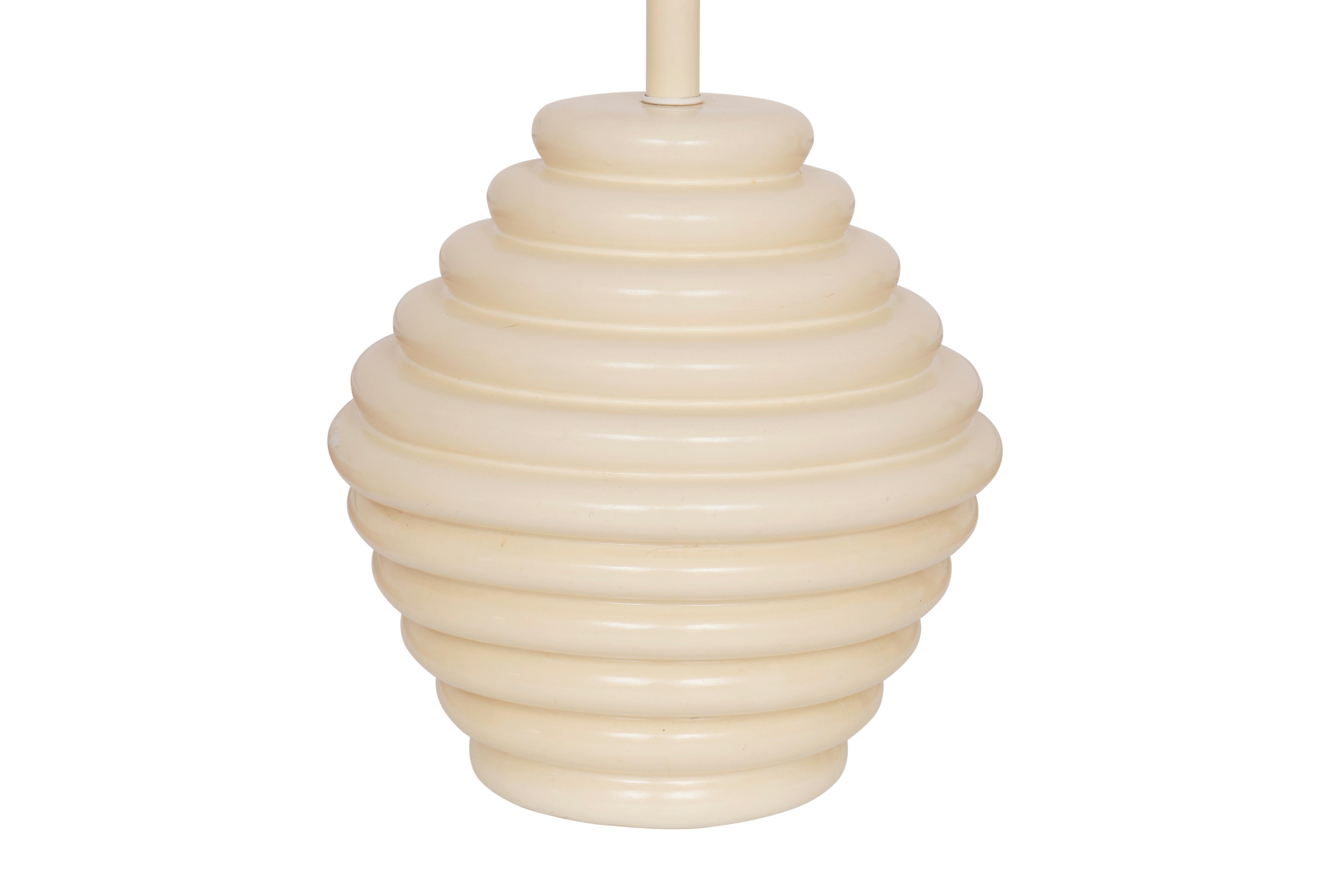 A round mid century ceramic table lamp in cream. Decorated with a ribbed texture throughout that gives the look of a beehive. Measures 18.75