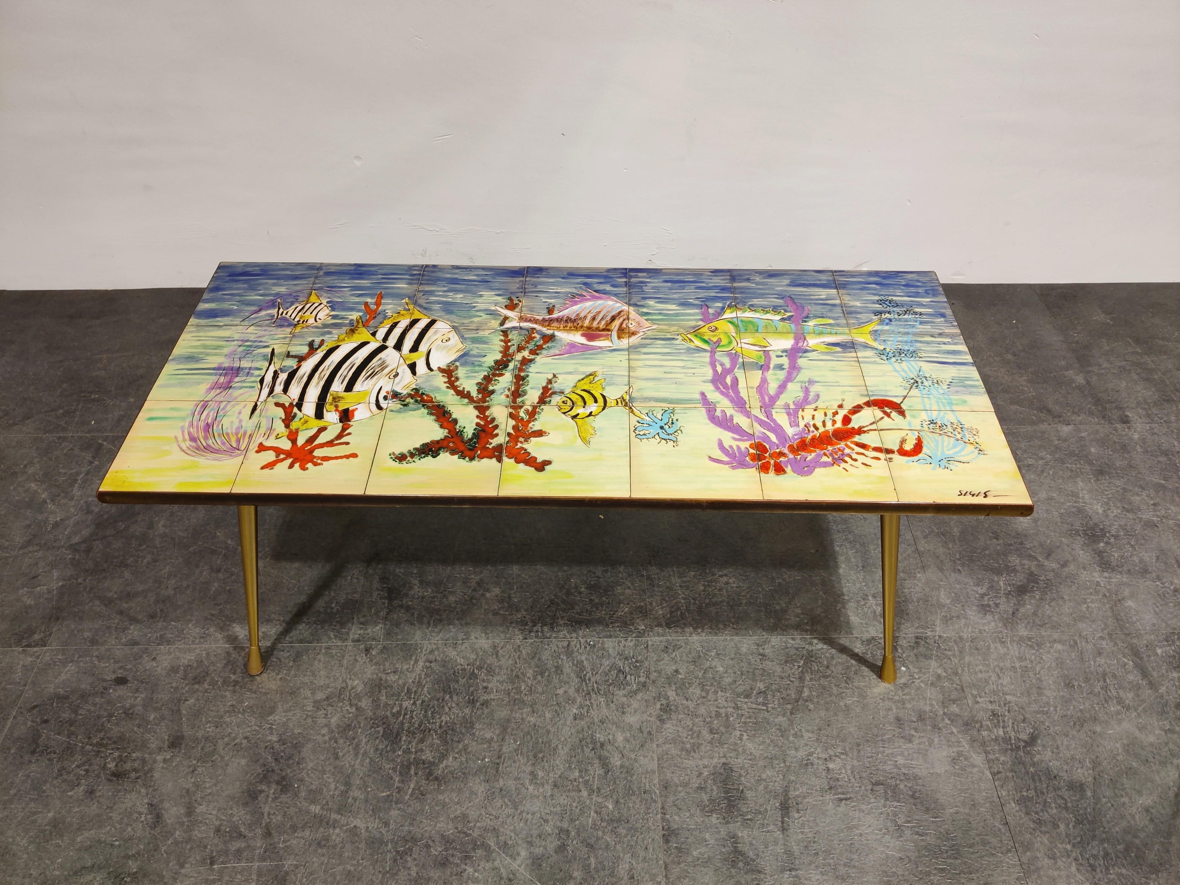 Stricking midcentury coffee table with a ceramic tiled top and elegant cast brass legs.

The table is signed by Sigis.

The coffee table depicts an underwater scene with very lively colors, a piece that really brings happiness.

Good