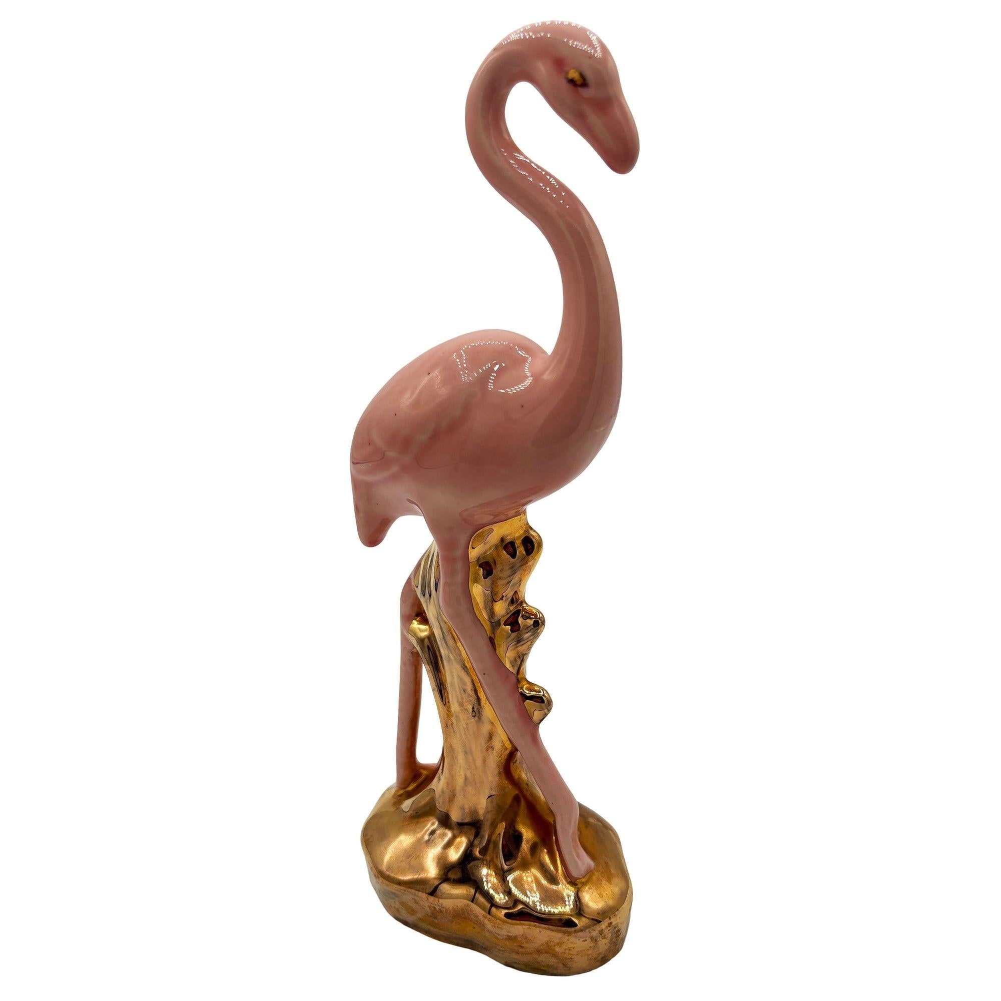 Mid-century pink and gold flamingo ceramic figurine. The statue features a pink flamingo with long legs, a slim, tall form standing on a grassy field, looking in curiosity. It comes in a gloss finish that highlights the rich pinks and