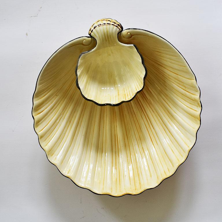 Ceramic clam shell serving platter in yellow, cream, and black. A beautiful addition to a table, this piece features two tiers. One clamshell at the top for dips or condiments, and a larger shell attached at the bottom for chips. The dish is oval or