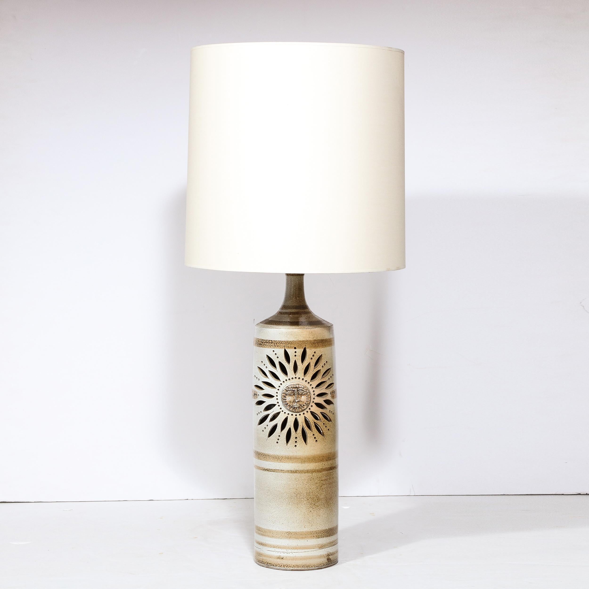 This refined Mid Century Modern ceramic handpainted table lamp was realized by the legendary Pierre Pissareff in France circa 1960. It features an mottled off white cylindrical body with horizontal ecru banding. A stylized sun motif sits the center