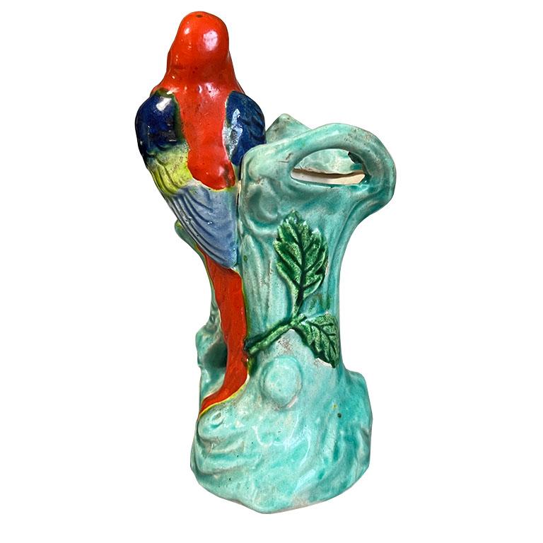 A small mid-century modern ceramic bird motif vase. This petite vessel features a bird perched upon a tree. He has red, blue and green feathers. The tree he sits upon is in green with red berries. The bottom is stamped with 
