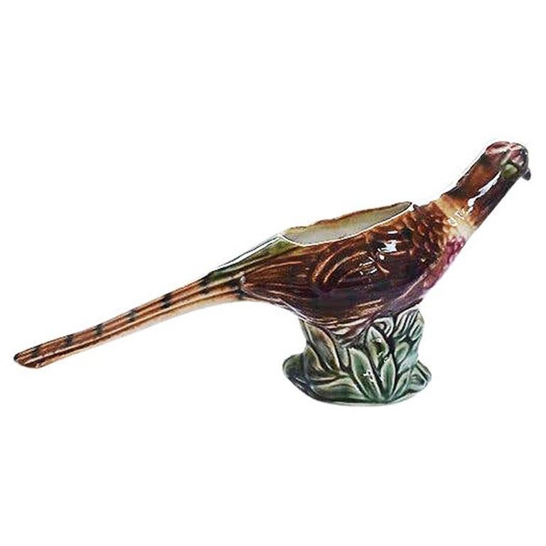 A beautiful glazed ceramic pheasant planter. This piece could be used as a vase or a small planter. The piece depicts a pheasant sitting upon a lush green patch of grass. His long tail and body are glazed in a brown and green design.