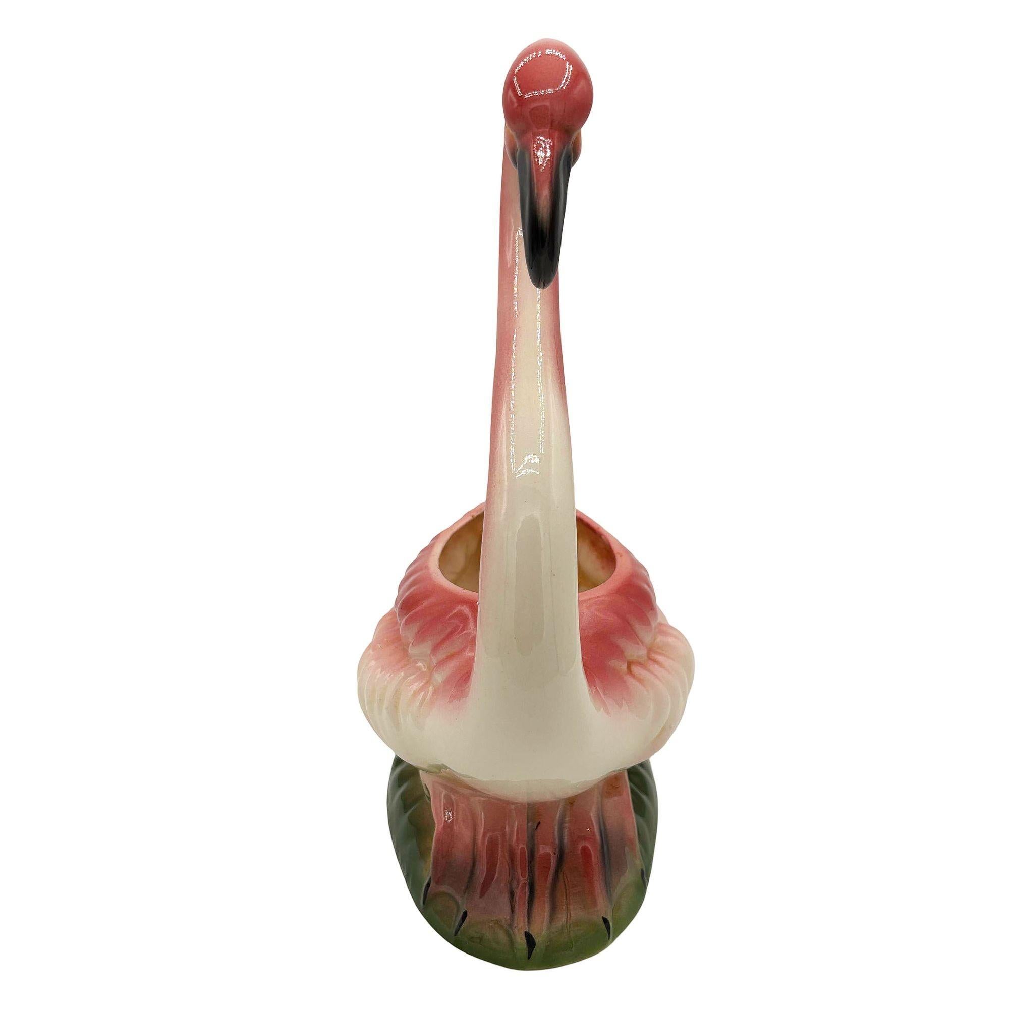 Mid-century pink and green ceramic flamingo tabletop California planter. The planter features a beautifully detailed pink flamingo resting on a lush green grassy field. It comes in a gloss finish that highlights the rich pinks, greens, and white