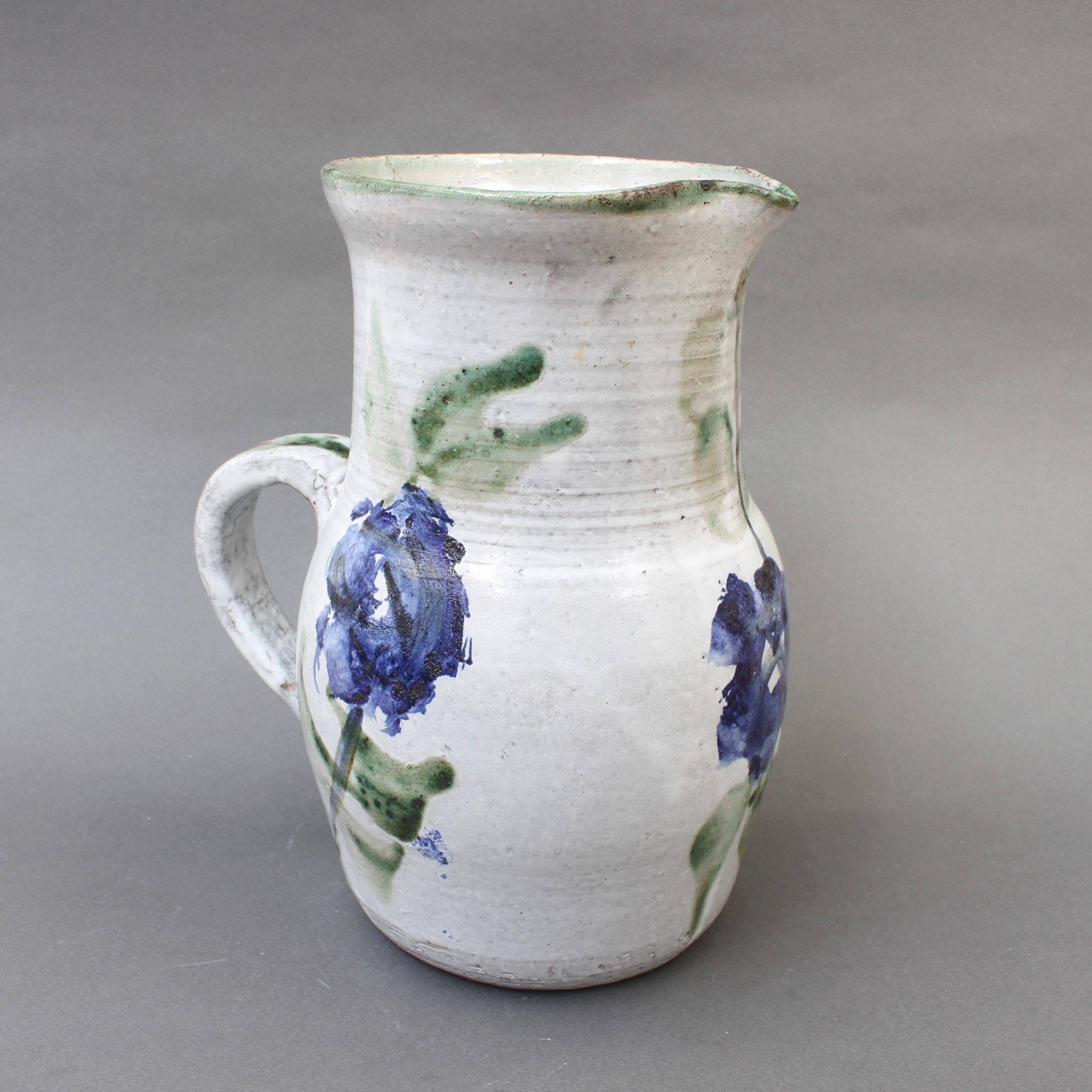 Midcentury ceramic pitcher (circa 1960s) by Albert Thiry (1932-2009). A classic Thiry design and decoration scheme, this pitcher's base color is done in a chalky-white glaze with painted blue flowers and trademark green leaves. It is elegantly