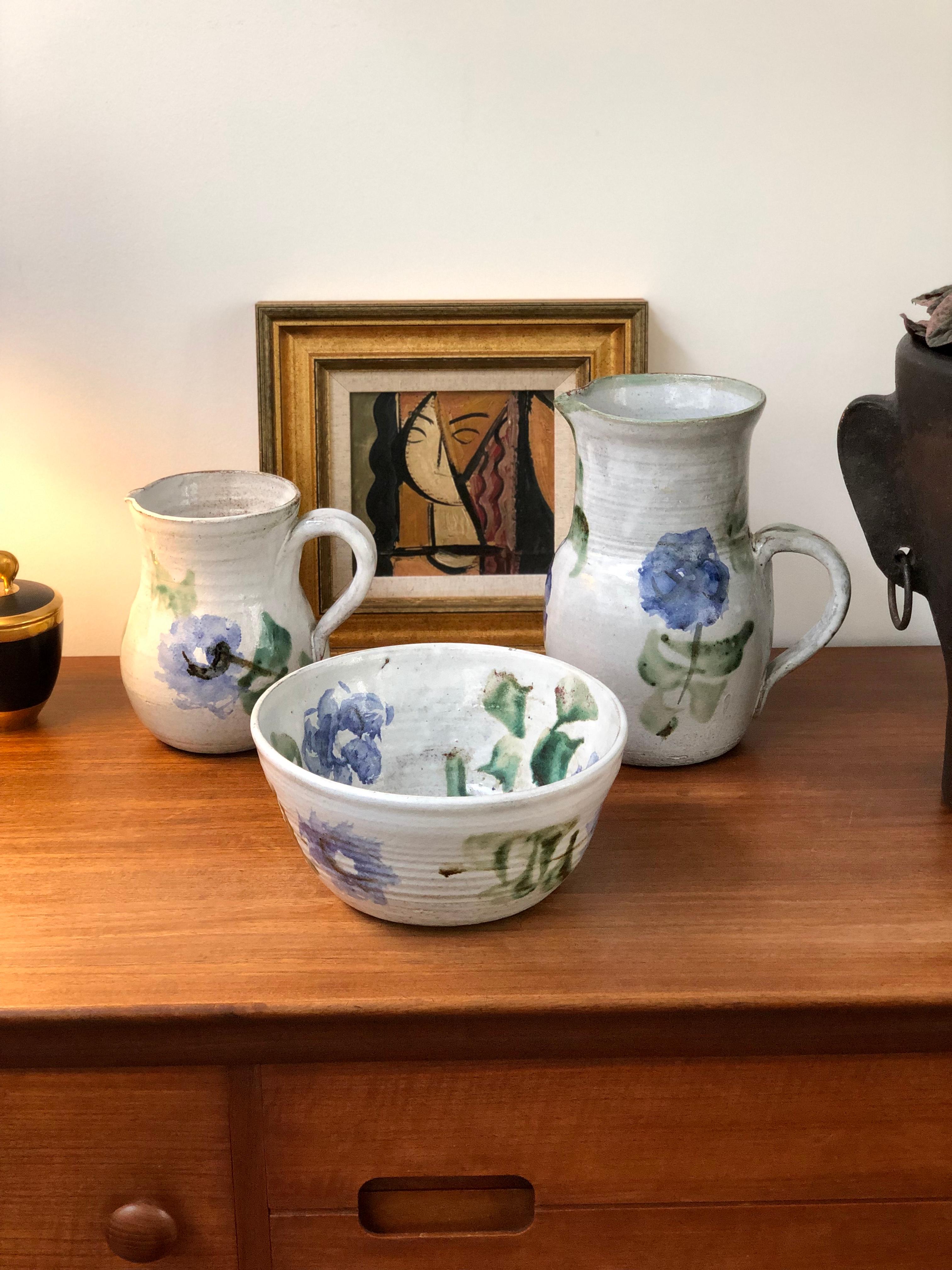 Midcentury ceramic pitcher (circa 1960s) by Albert Thiry (1932 - 2009). A classic Thiry design and decoration scheme, this pitcher's base color is done in a chalky-white glaze with painted blue flowers and trademark green leaves. It is elegantly