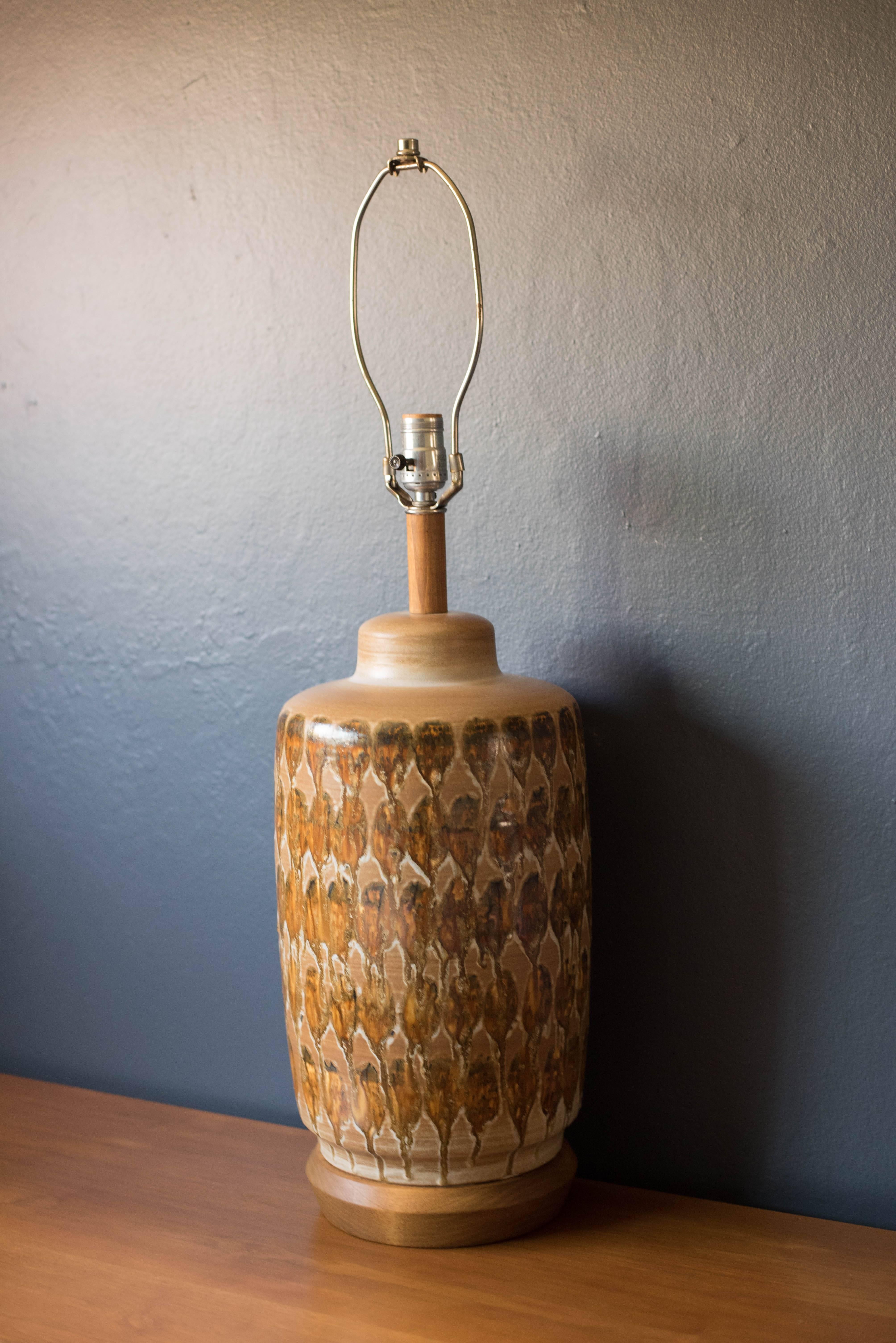Mid-century ceramic pottery lamp, circa 1960s. This piece has a drip glazed finish in neutral tones. Features a three way switch and walnut stem and base.
 