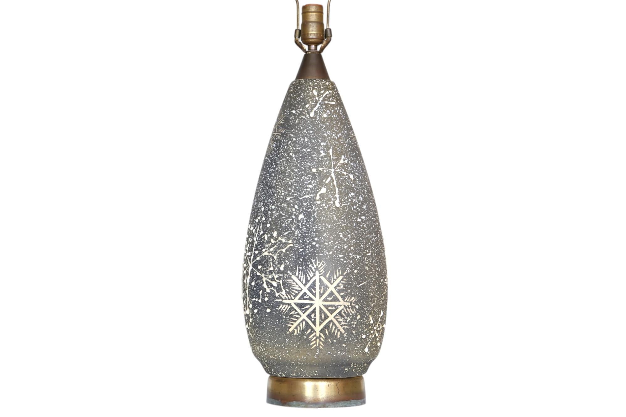 A mid-century production piece table lamp. The charcoal gray ceramic body is incised with a star or snowflake motif, and is decorated further with speckled raised white glaze, some of which is also in the same star motif. The vase is surmounted with