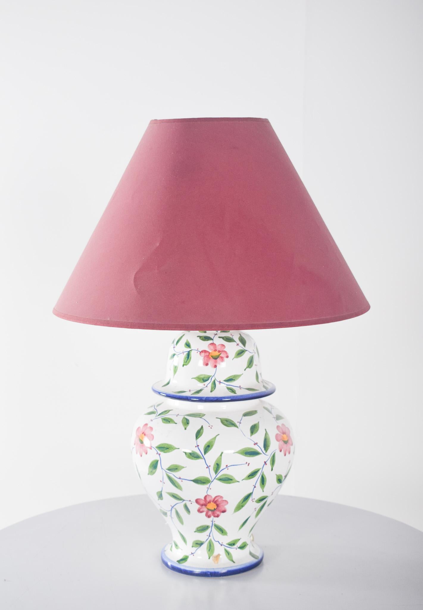 Ceramic table lamp in the shape of a pot. Handmade polychrome decoration with floral motifs. The flowers are painted in shades of pink and red, accompanied by carefully hand-painted green leaves and thin branches.
The outline of the base and the top